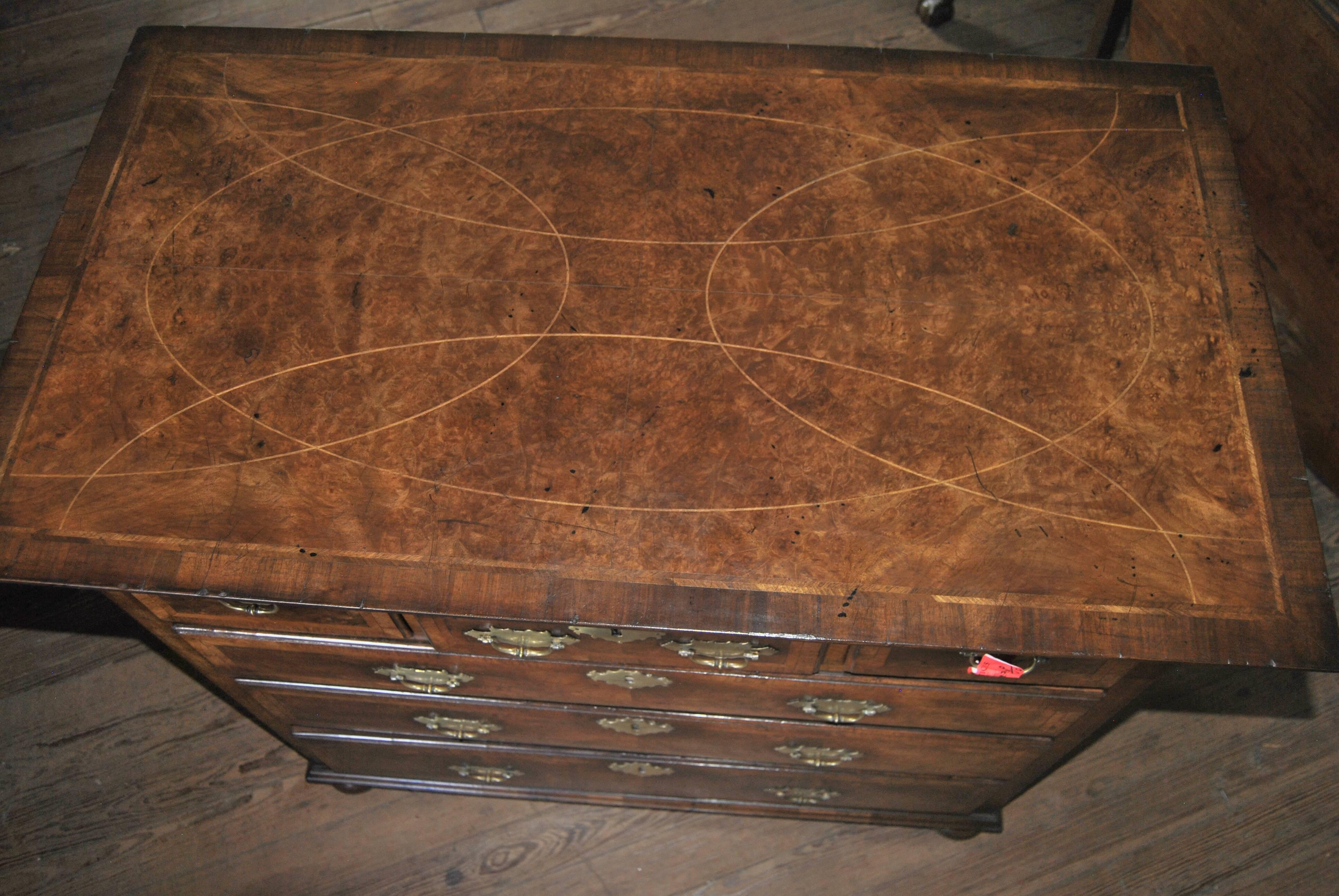 This is a walnut and Kashmir walnut chest of drawers made in England, circa 1750. There is an overhanging top over a cross cut layered molding. There are three drawers over three drawers. Each drawer has a walnut outside edge with a walnut banding