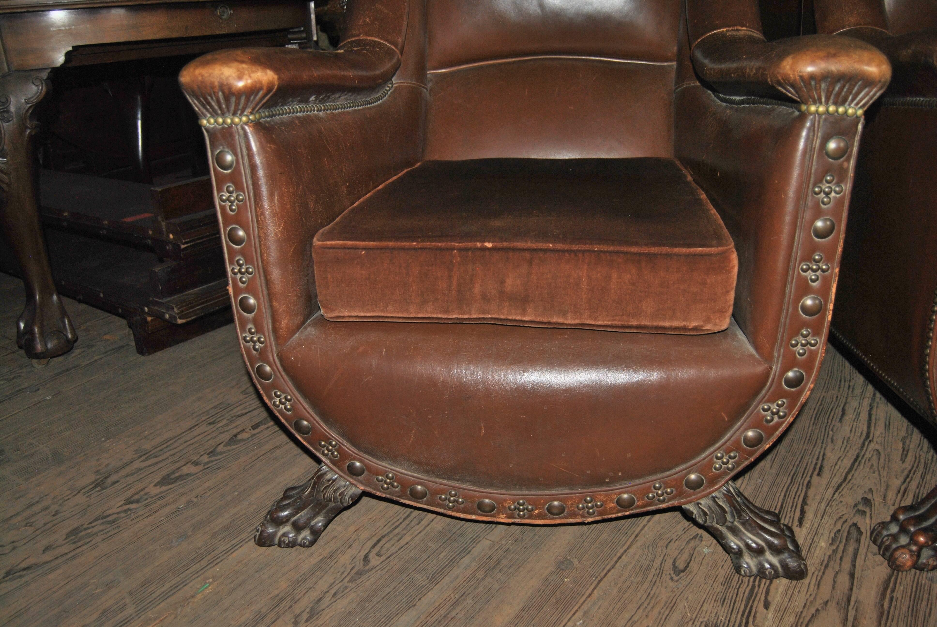 This is a pair of leather English club chairs made circa 1925. The leather is a beautiful rich brown color. The seat cushion is in a complimentary brown material. The chairs have a stunning U shape to the front. The fronts of the chairs have brass