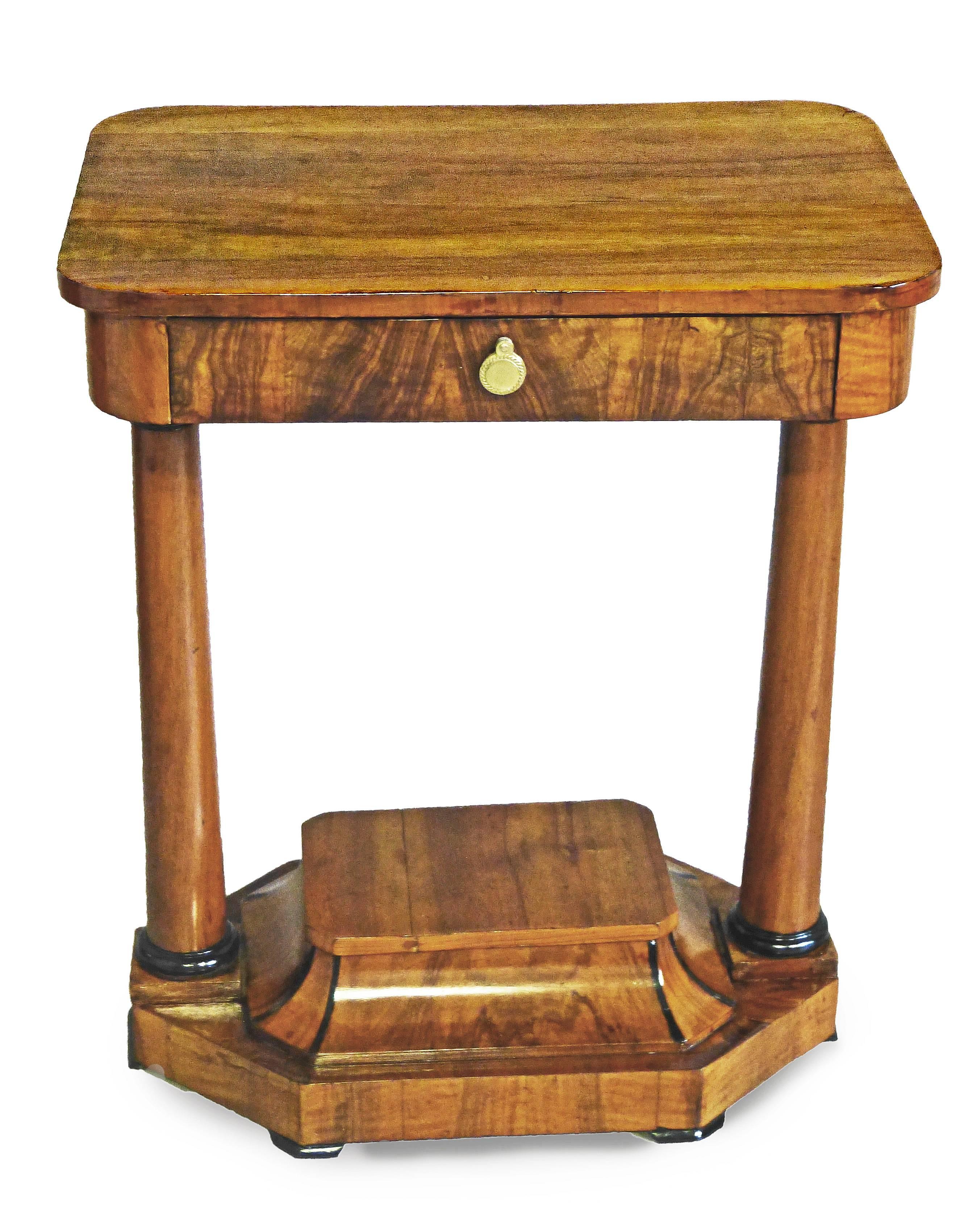 Biedermeier sewing / work table of figured walnut and of unusual design supported by 2 reverse tapering columns with ebonized tops and bottoms. The main part of rectangular shape with rounded corners, all supported by a base with ebonized trim