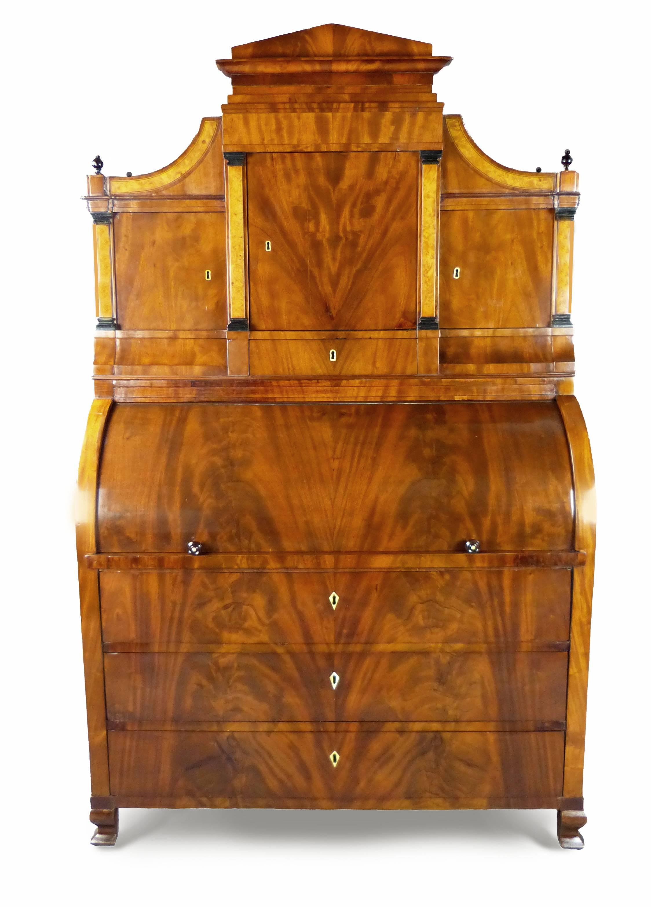 Fine and iconic figured mahogany Biedermeier cylinder bureau/secretaire with architectural top consisting of a central door flanked by two further doors all with applied birds eye maple columns with ebony capitals and drawers below, two of them