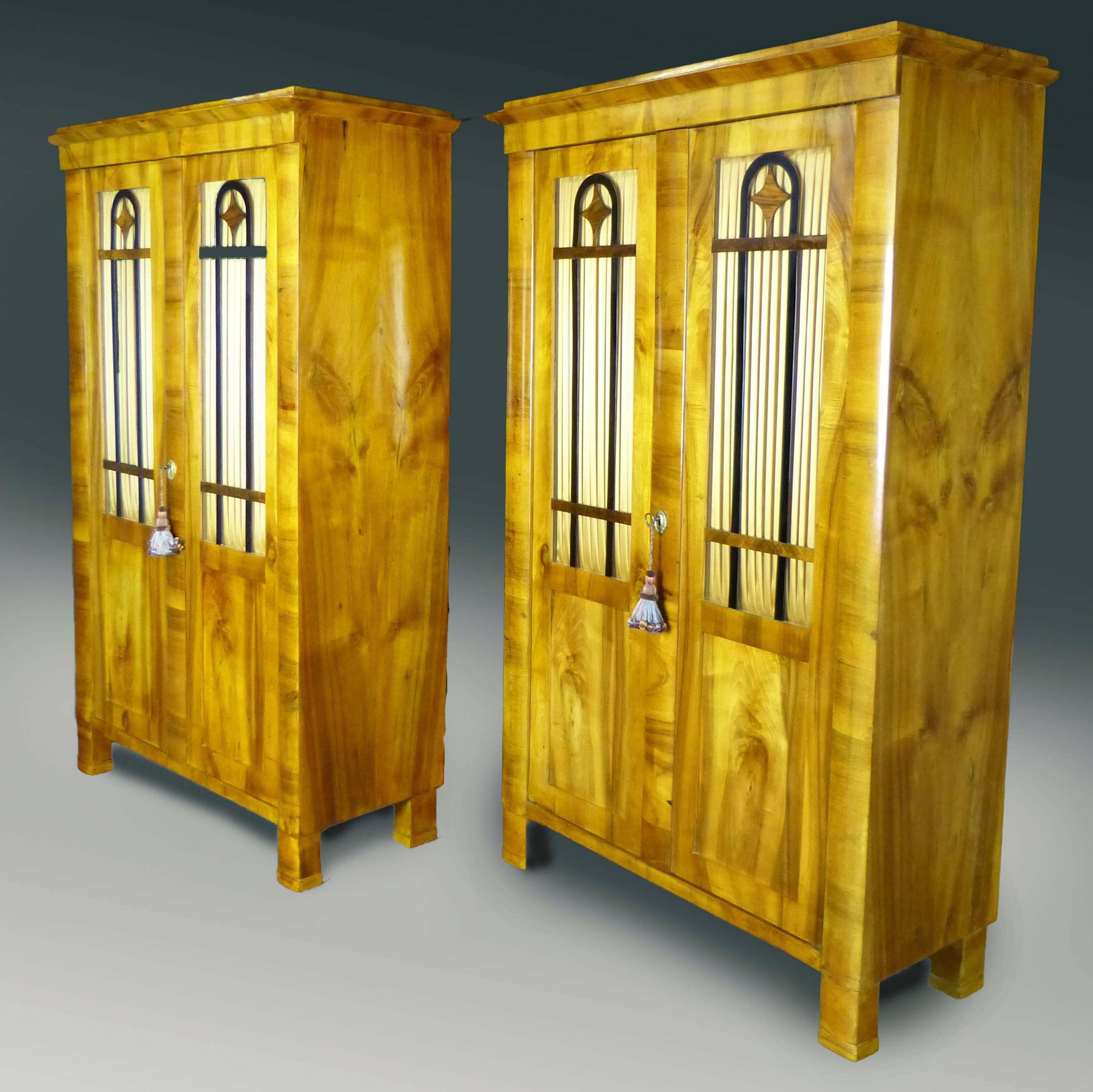 Outstanding and rare pair of period Biedermeier display cabinets / Bookcases of finely figured north European blond walnut exterior. Each display cabinet features three slightly curved frontal columns, two of them terminating below in block feet of