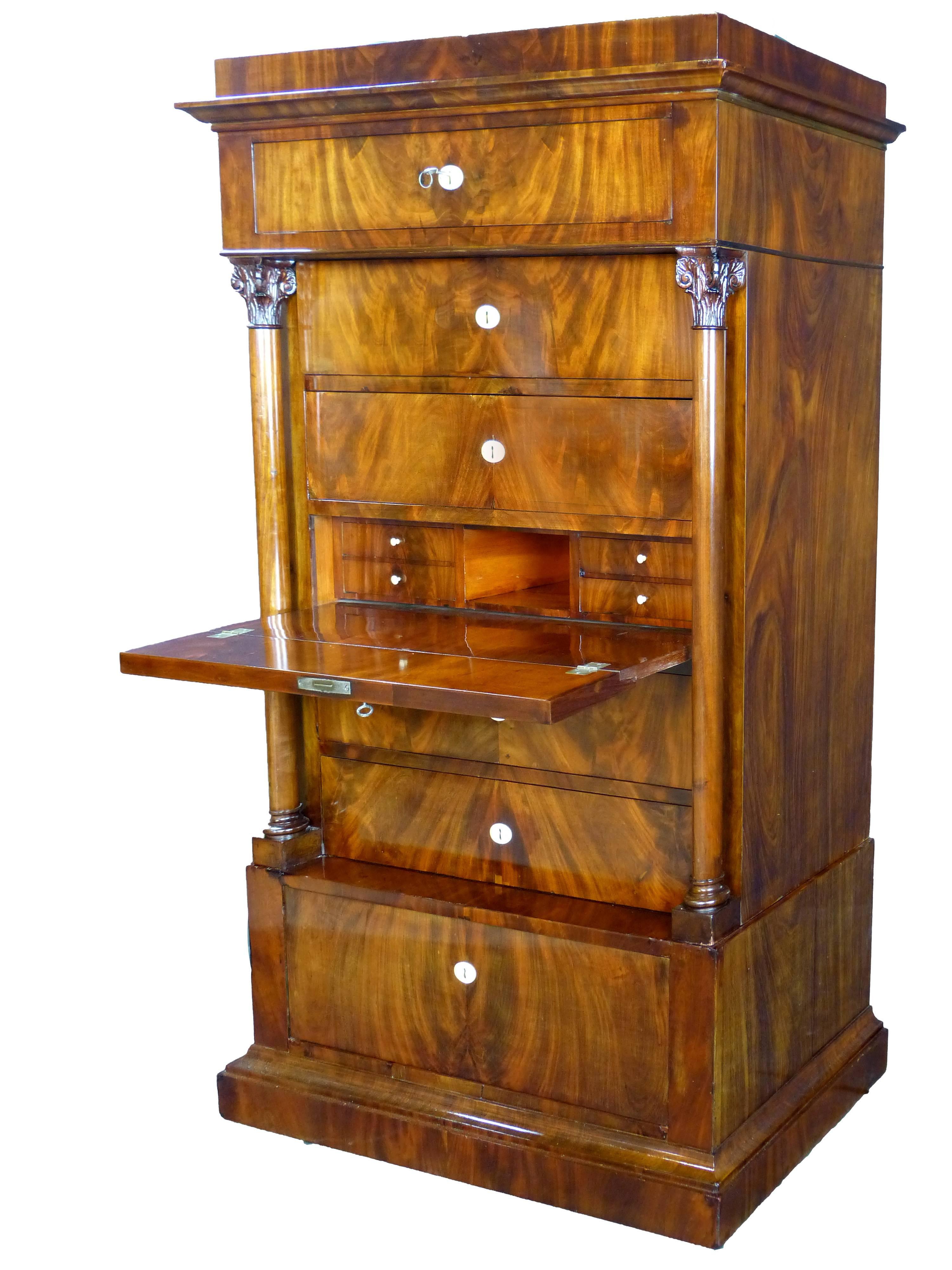 Elegant commode semainier Biedermeier of Danish origin dating to the middle of 19th century of exceptional figured mahogany veneers and solid oak interior. The two frontal columns have Corinthian capitals. One of the seven drawers serves as a bureau