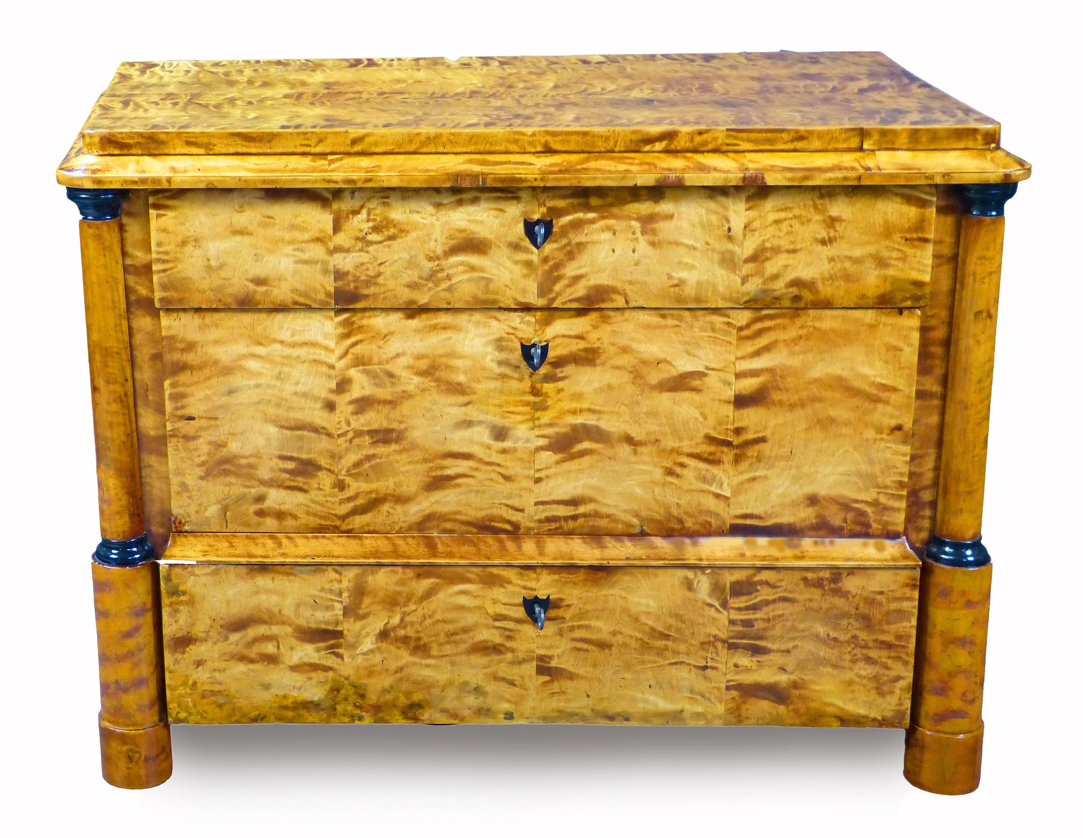 Unusual early 19th century, North German Biedermeier commode of fine tiger maple veneers in their natural color. Two frontal columns with ebonized ring capitols flanking 3 drawers of varying size and shape with black buffalo horn escutcheon