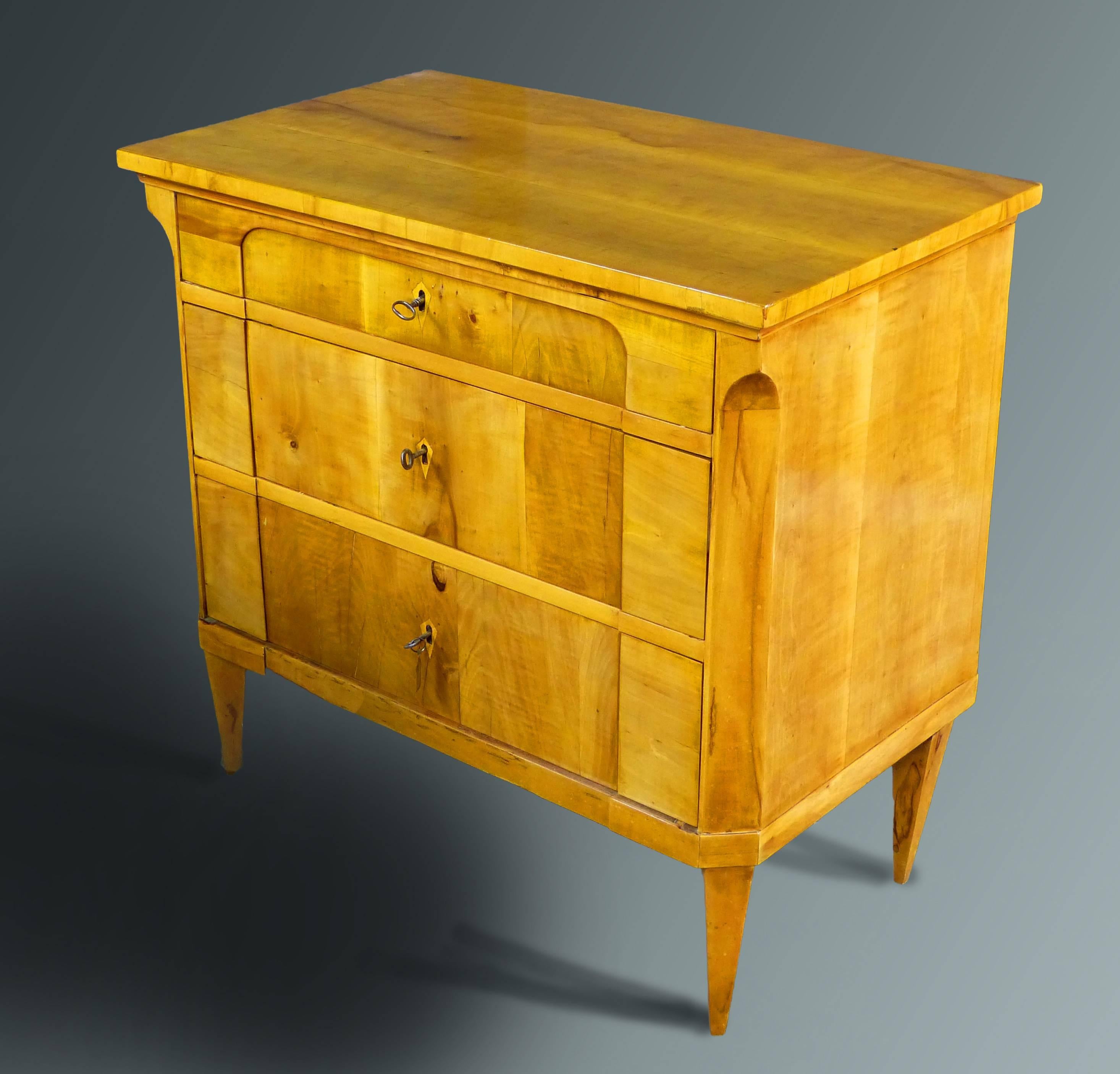 Petit Biedermeier Austrian Commode of satin birch veneers with an architectural front and canted corners, the upper drawer opens to reveal a writing surface, leather lined, with interior storage compartments and a center that can be used as a