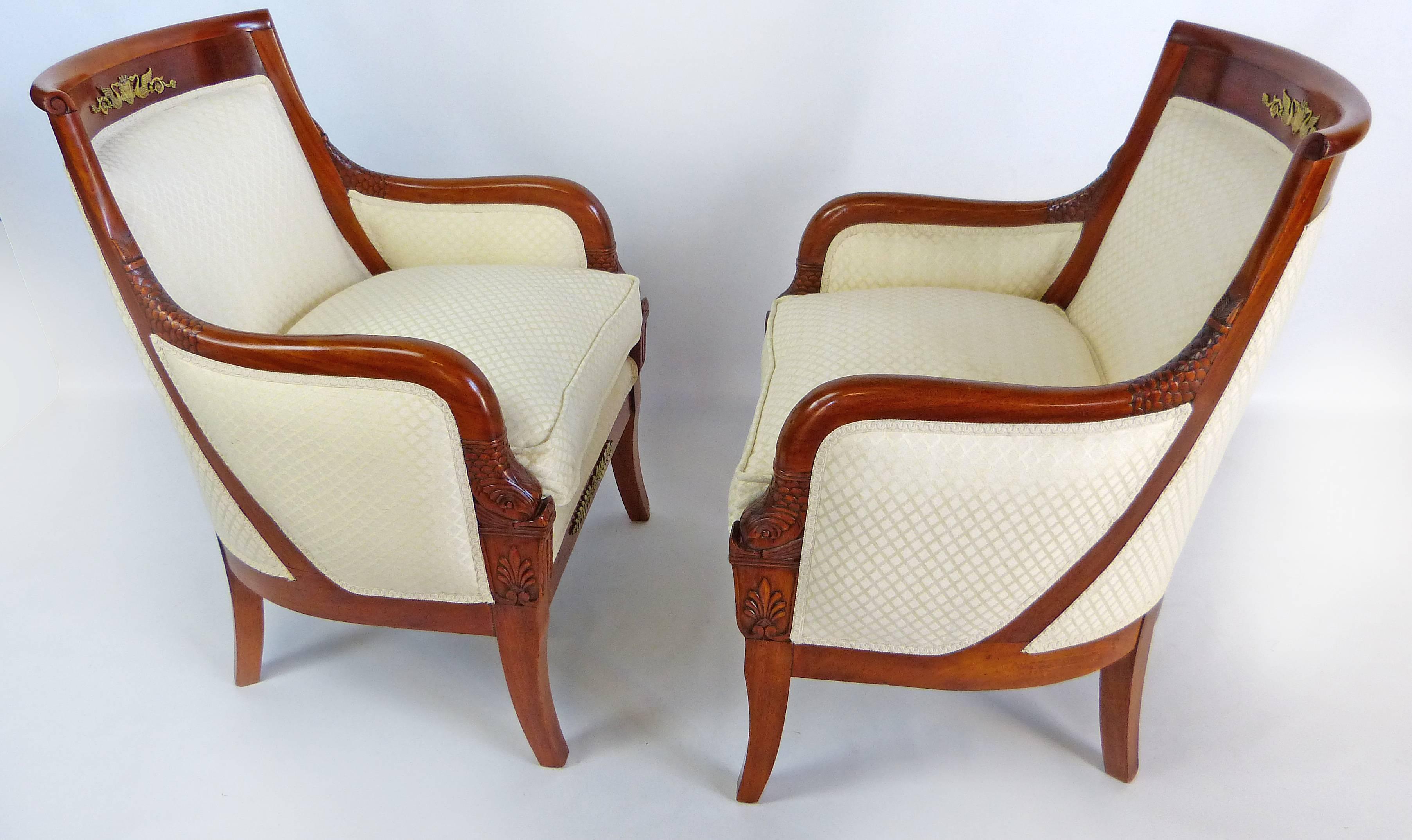 Fine pair of early 19th century Empire armchairs with round backs and pillowed seats. Made of solid mahogany they are sturdy and very comfortable. There is intricate and masterful carving at the top of the arms imitating fish scales and tail