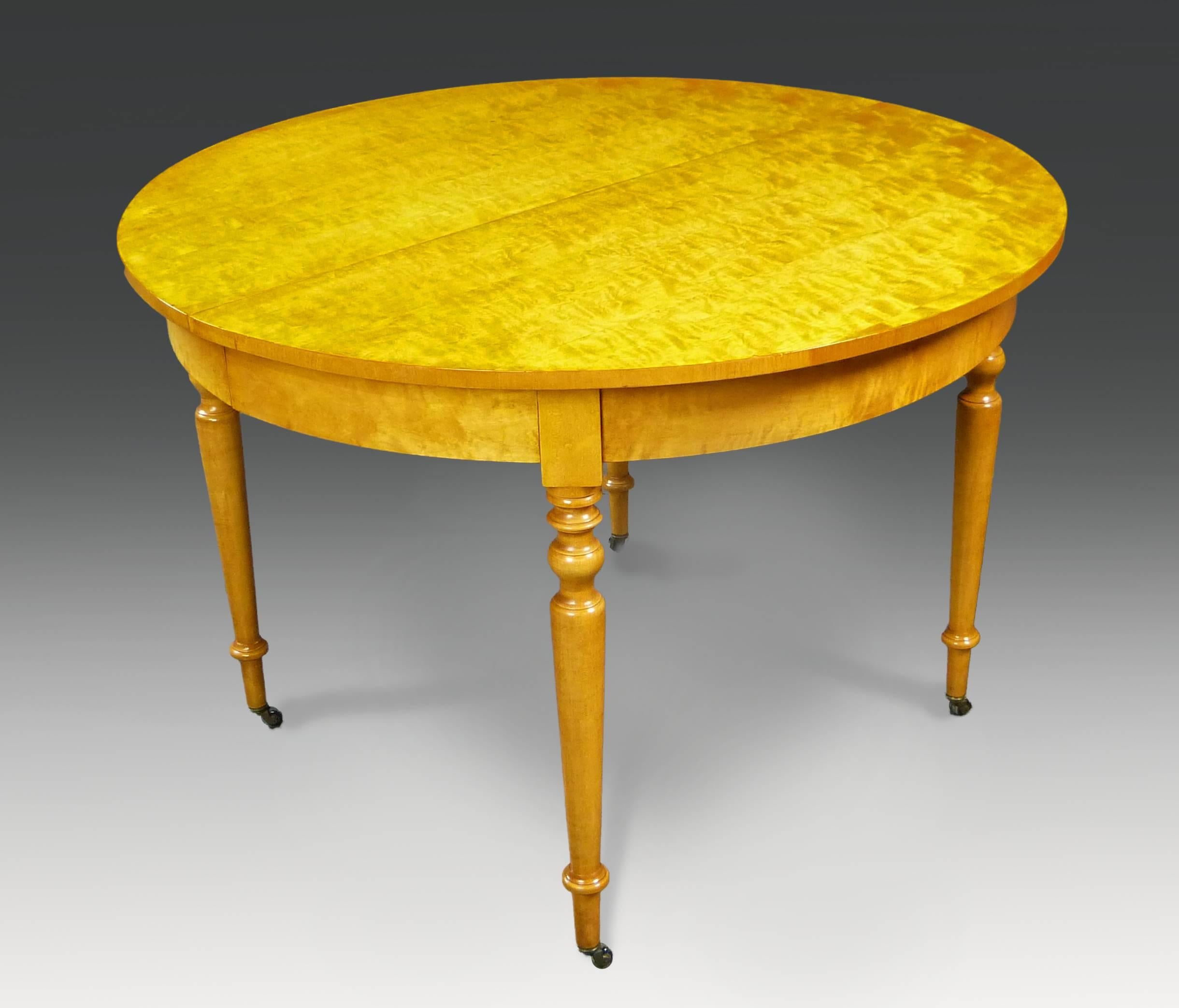 Attractive end of 19th century Biedermeier Revival circular dining table with two skirted extension leaves. It is made of fine quilted birchwood veneers with four finely turned solid birchwood legs terminating in casters. The interior structure is