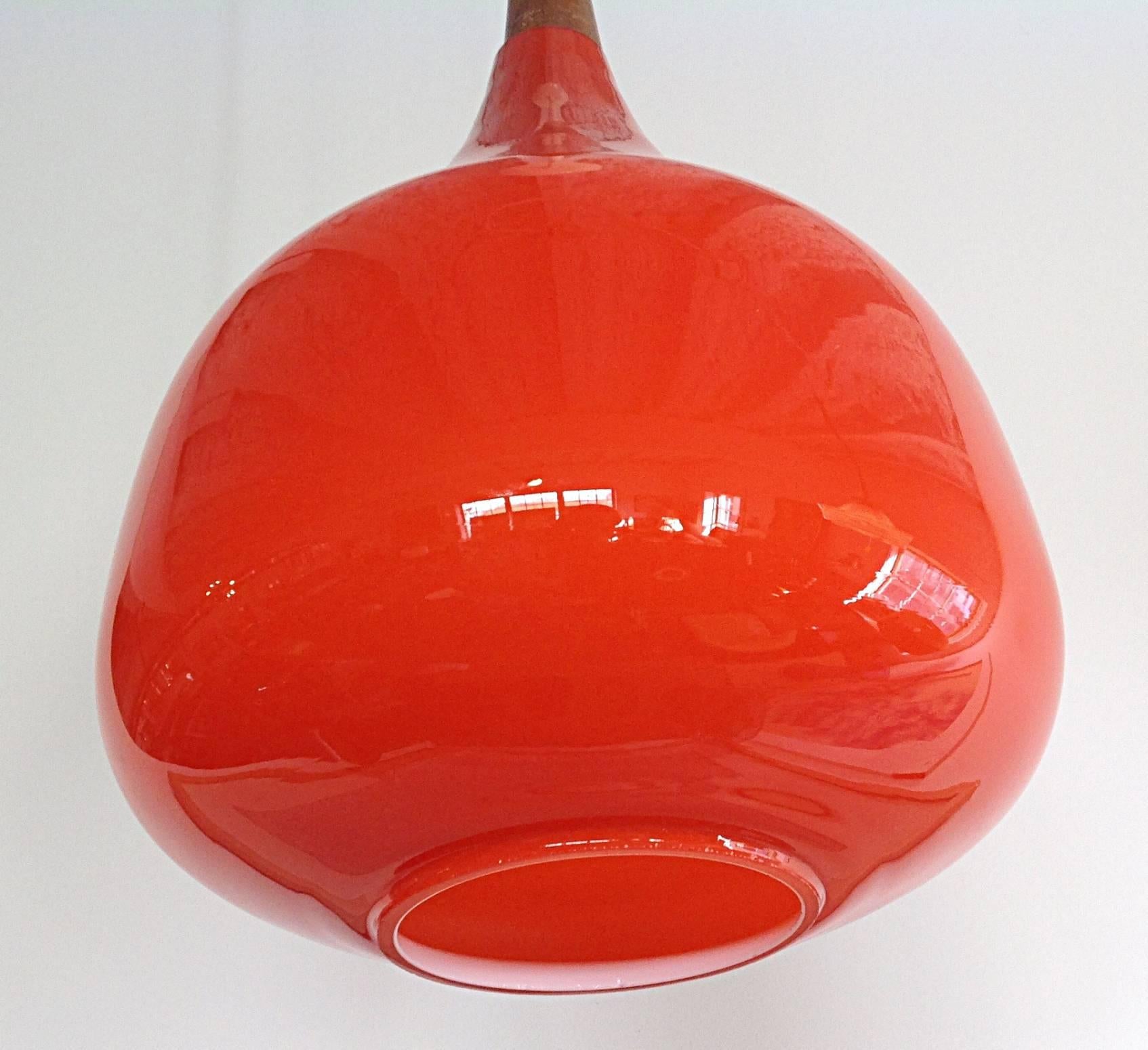 Rich tomato color cased glass, onion shaped pendants by Luxus. Each glass pendant is topped with a wooden conical finial which the cord travels through. Retains original white ceiling caps. Overall drop is approximately 36