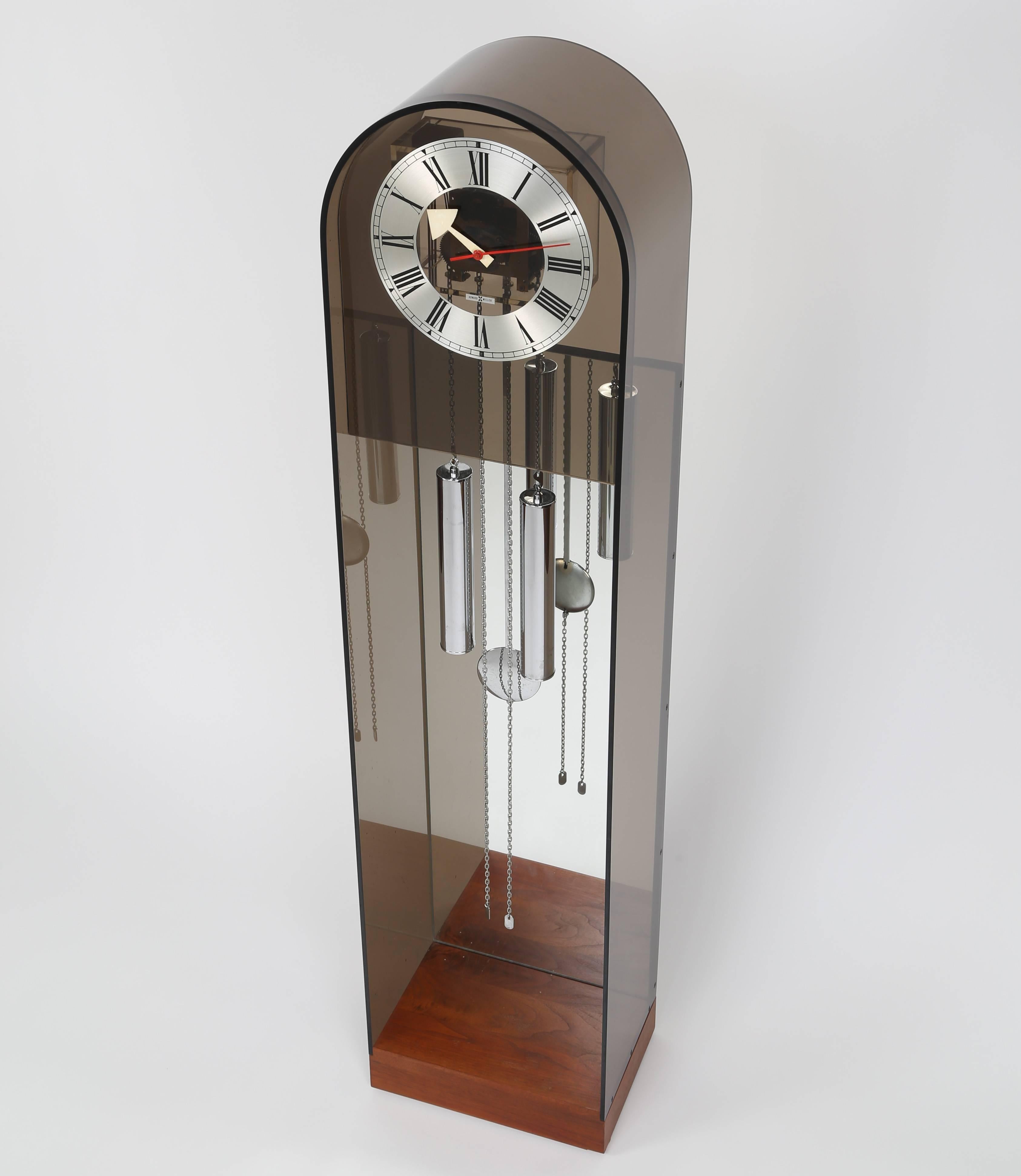 Howard Miller tall case clock in smoked Lucite with a walnut base, mirrored back, and chrome weights and pendulum. Mechanical movement is driven by traditional weights on chains. Howard Miller, Zealand, MI, USA, circa 1970s. Manufacturer label.