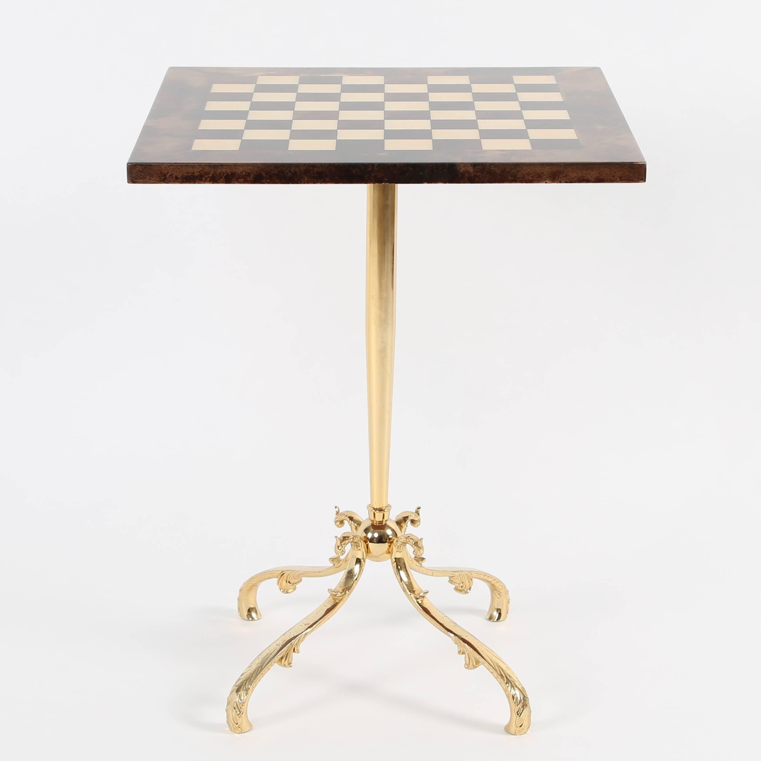 Square games table with a checkerboard top in tan and dark-brown lacquered goatskin, raised on a single polished-brass stem anchored by four ornate feet. Unmistakable Tura styling, signed with 