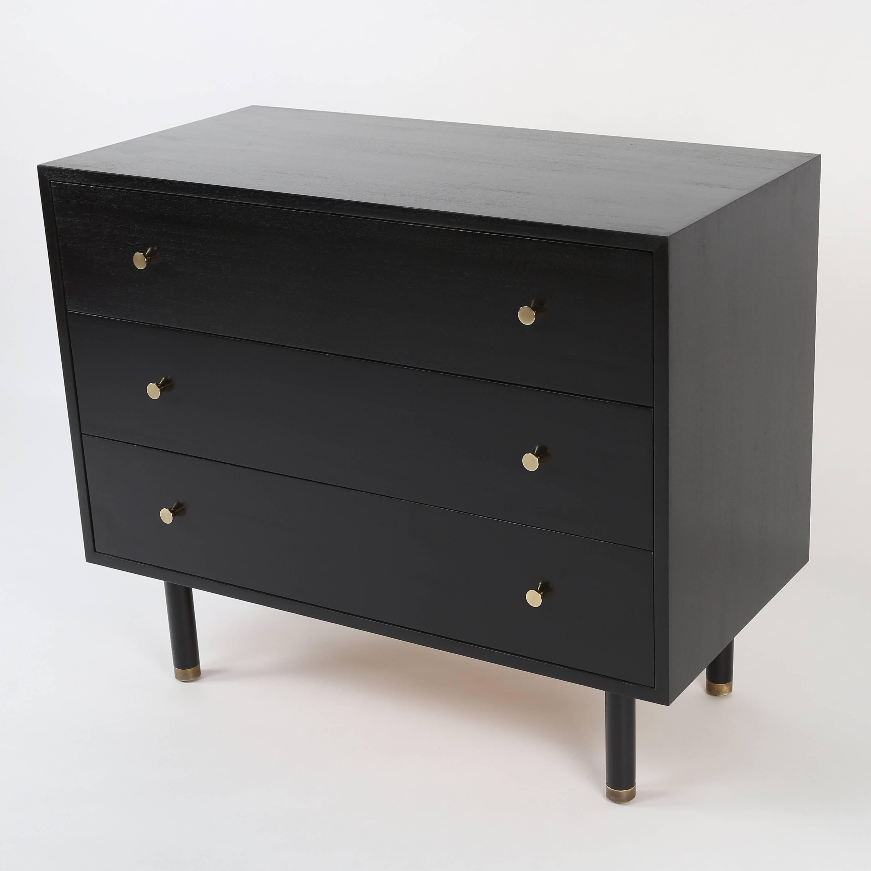Three-drawer Harvey Probber chest in ebonized mahogany, resting on four circular legs with brass-capped feet, circa 1950s. Each drawer features two solid brass pulls. Top drawer has two removable dividers. Harvey Probber label on inside of top