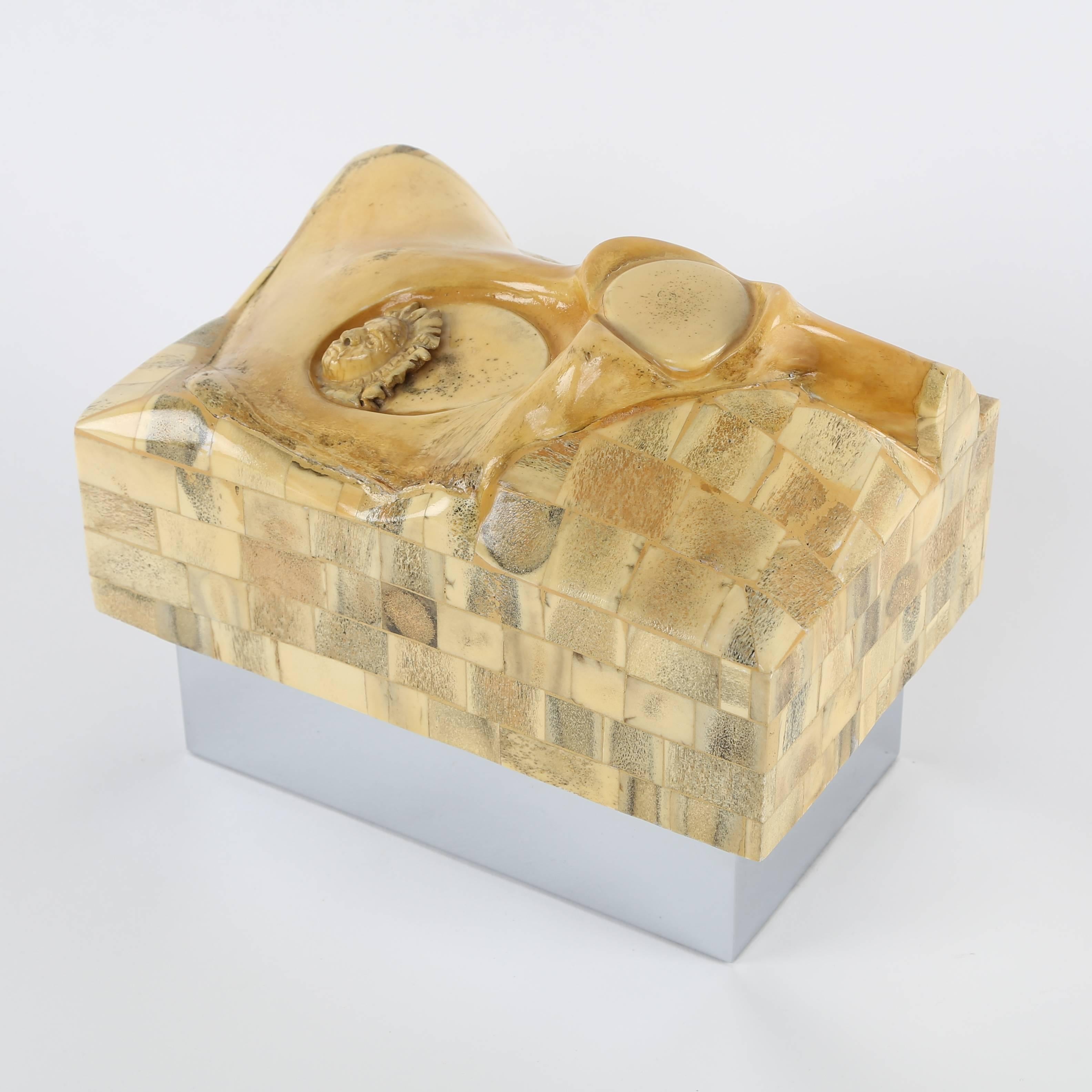 A conversation starter if ever there was one, this rare and unusual 1970s box features a large bone as well as a small face carved from bone. The sides of the top are covered in tessellated bone tiles. The base is nickel-plated steel, and both the