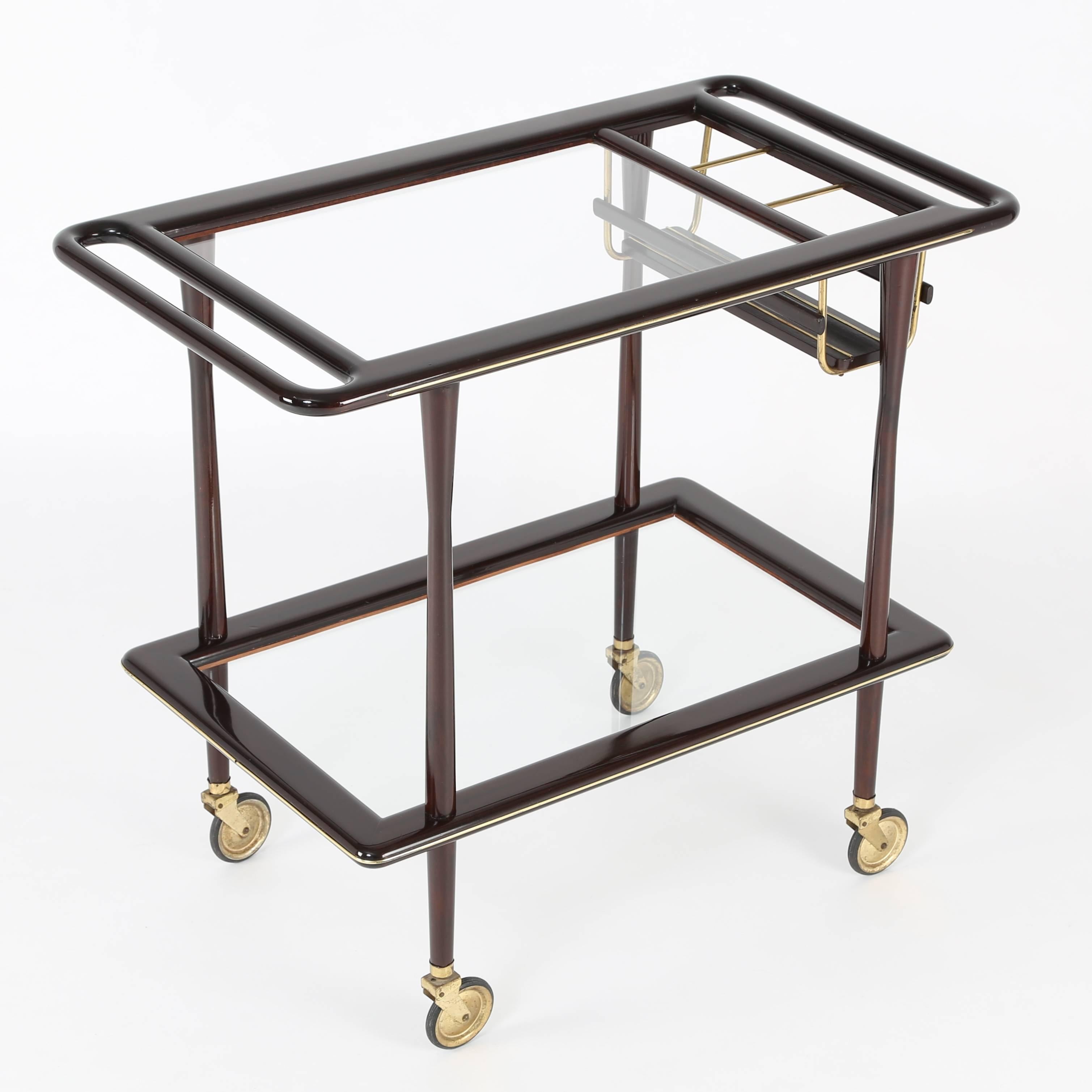 Versatile two-tier Italian bar cart in mahogany, brass and glass attributed to Cesare Lacca, circa 1950s. Upper shelf has a bottle rack for wine or spirits, with handles on both sides for easy movement on four wheels. Frame is made of highly