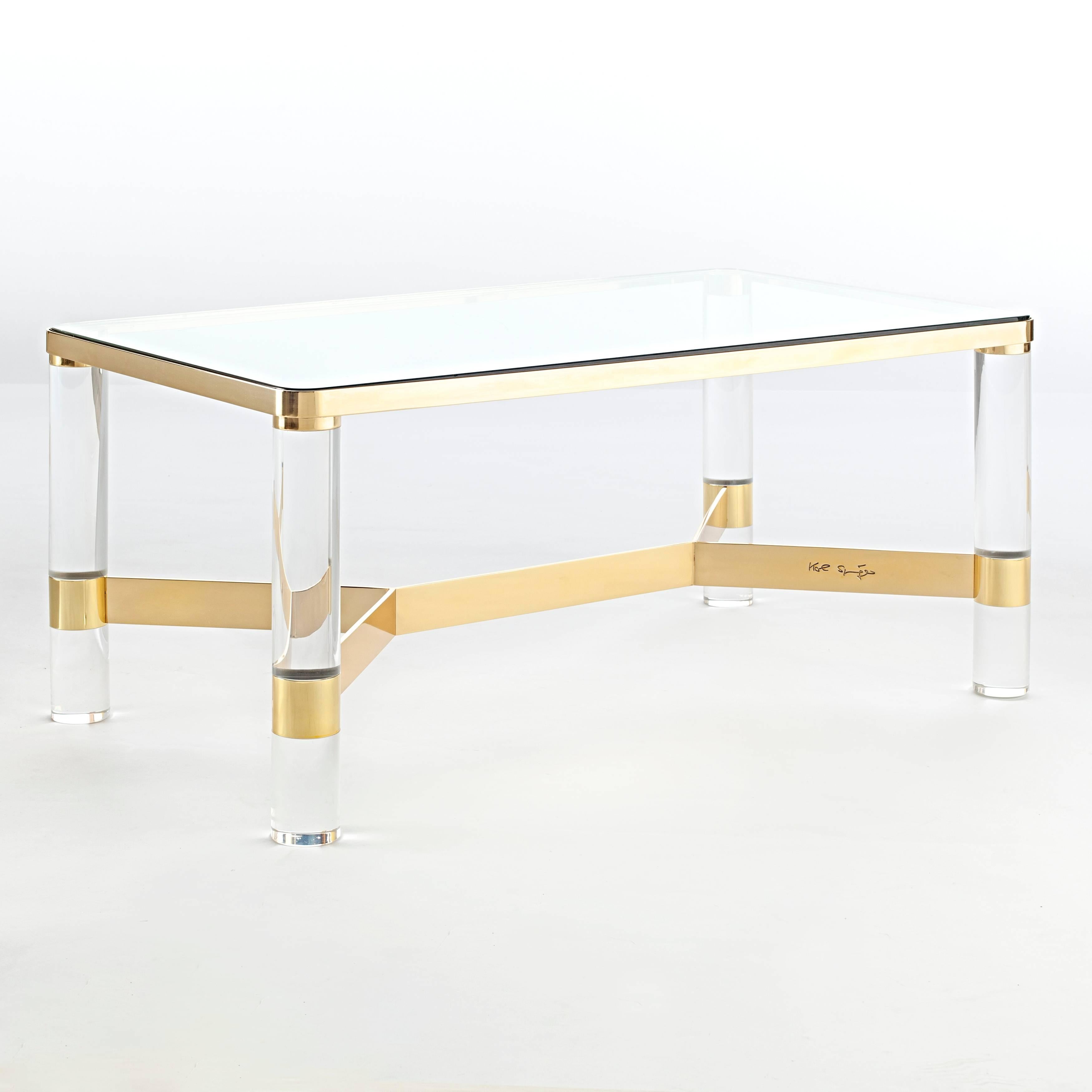 This chic 1980s cocktail table showcases Karl Springer's typical high-quality of construction and attention to detail. The four thick and chunky Lucite legs are held together by a four-arm stretcher; a brass frame above supports the glass top. The