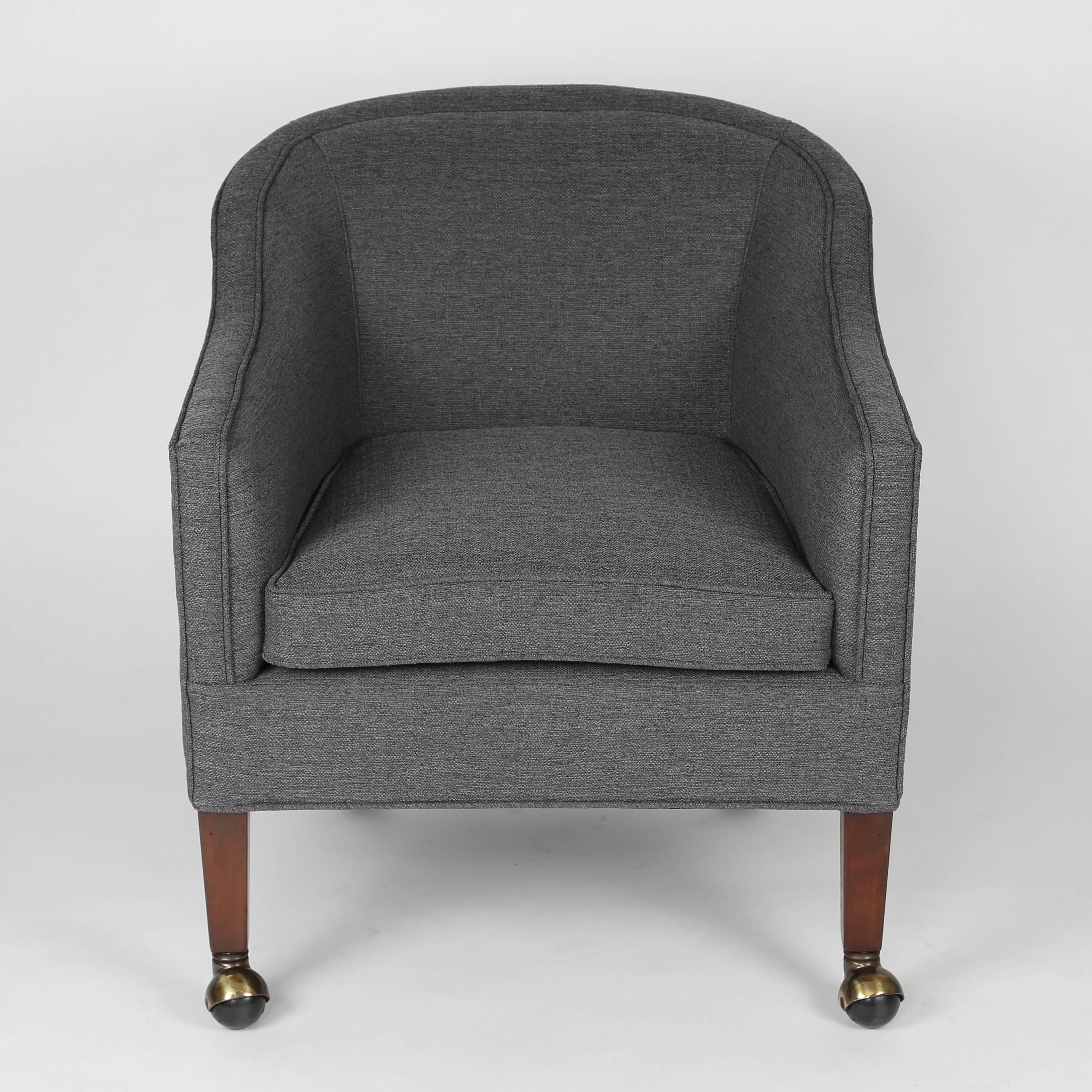 Well made lounge chairs with a loose seat cushion and fully upholstered body, featuring sloped arms that graduate to a rounded back frame. Newly upholstered in grey woven fabric. All four mahogany legs on casters. We don't know who designed these