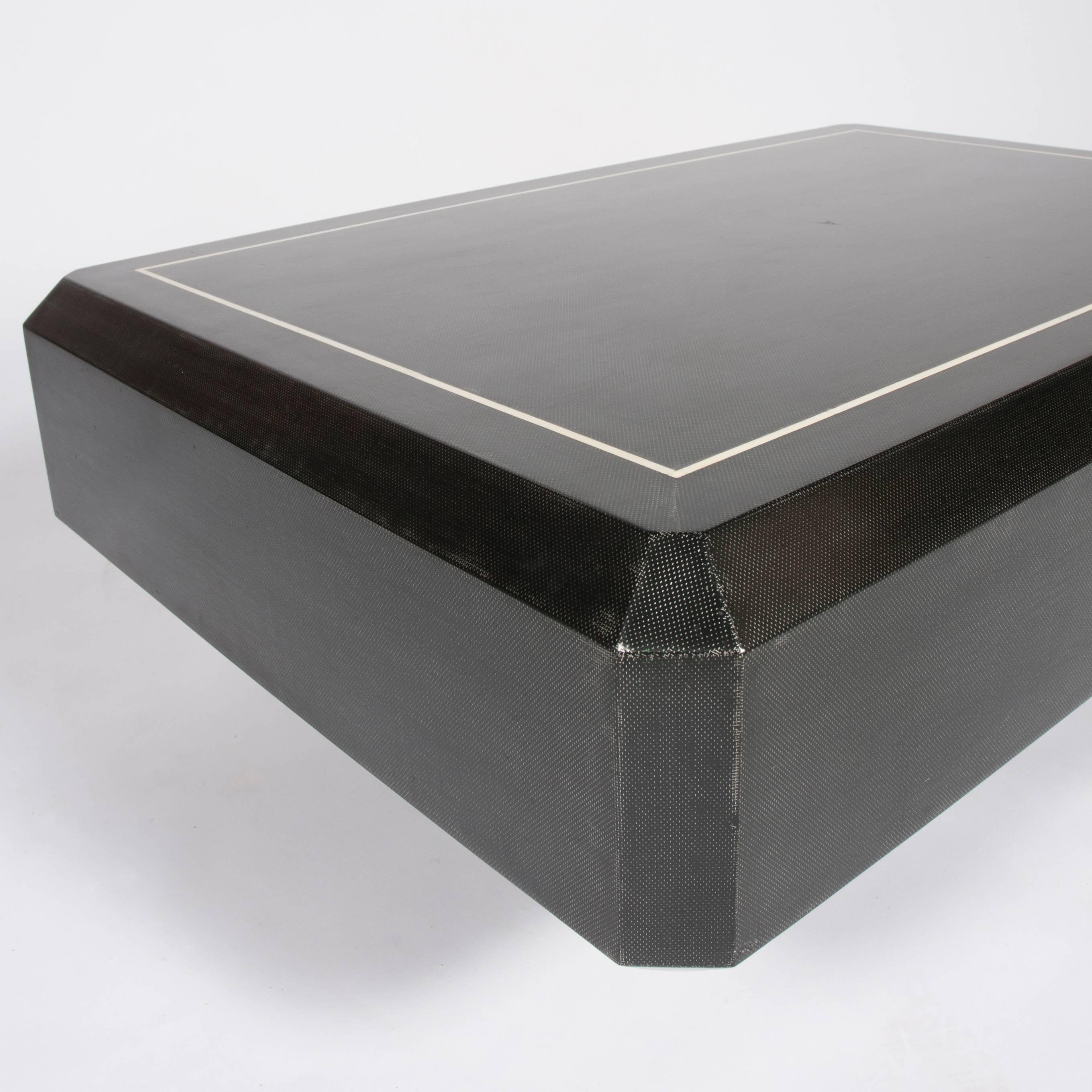 An unusual 1970s, Karl Springer coffee table with a faceted, rectangular top covered in lacquered black linen fabric with inset bone trim, over a recessed pedestal base illuminated by four lights. 



