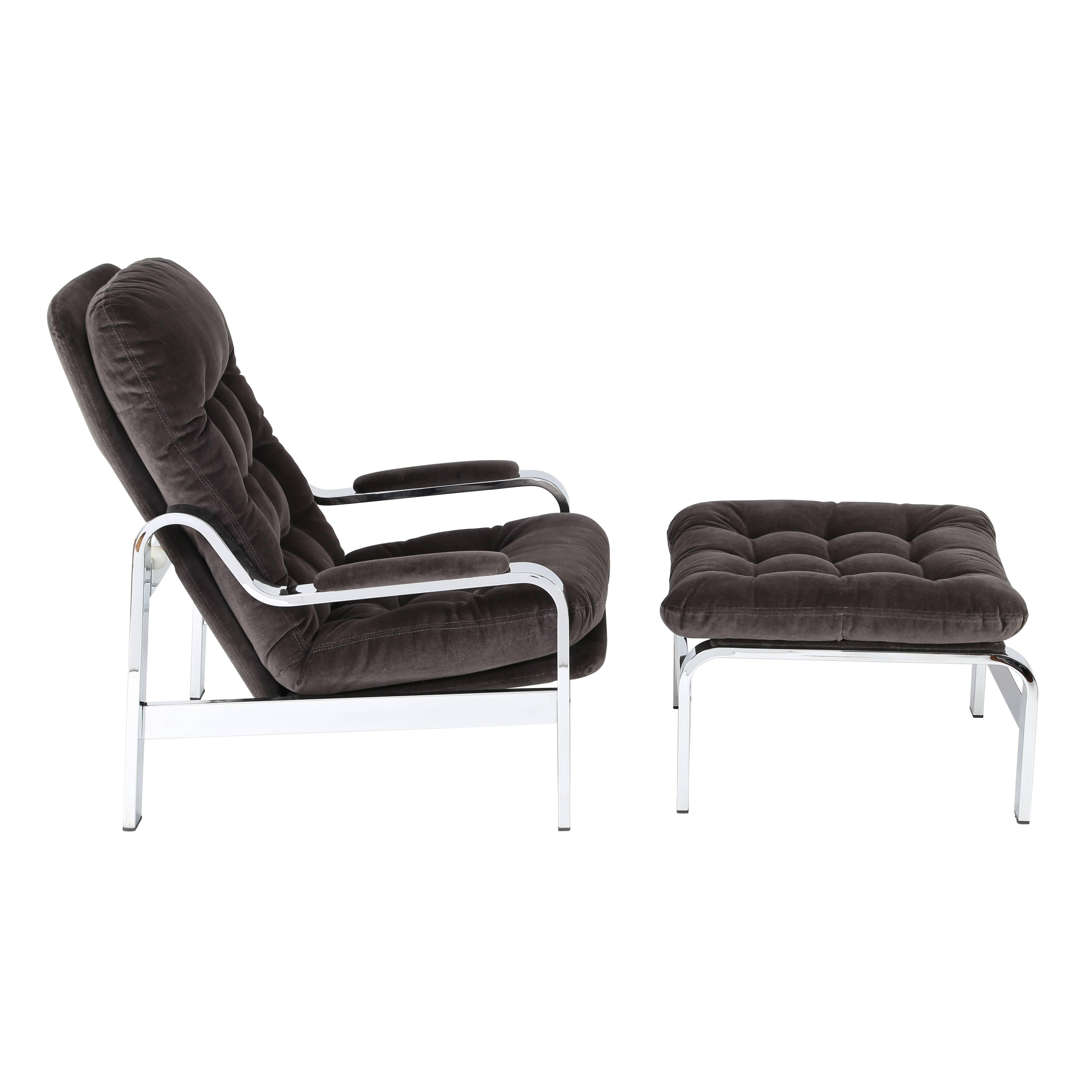 This extremely comfortable reclining armchair and ottoman are beautifully made with heavy, substantial chrome frames. The chair can smoothly slide back into a semi-reclined position. Newly reupholstered in a warm dark-grey cotton velvet. We do not