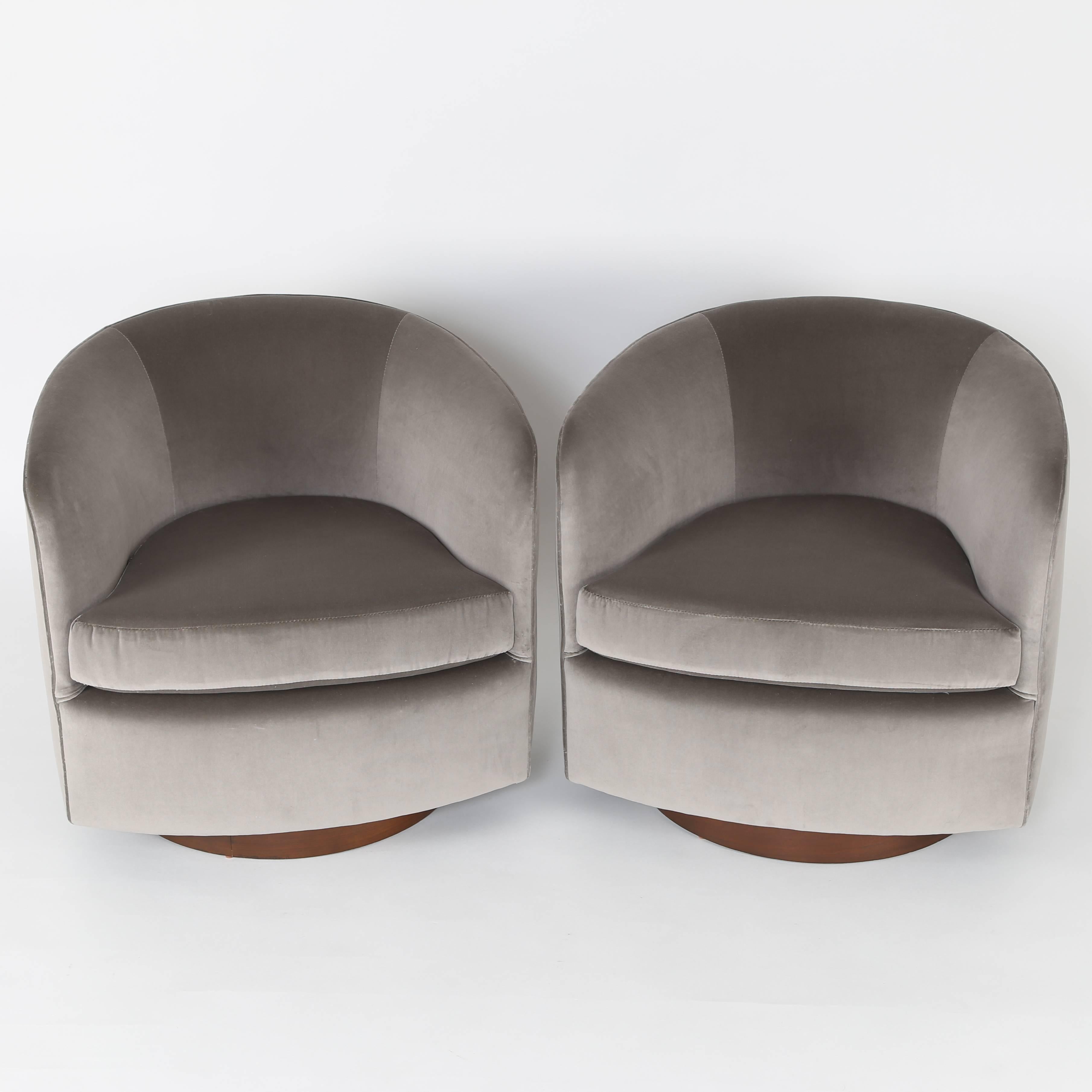 Chic and versatile pair of tilt and swivel armchairs by Milo Baughman for Thayer Coggin. These comfortable chairs rotate on round, walnut-clad bases. This pair has been reupholstered in a luxurious, soft, medium-gray cotton velvet with warm tones.