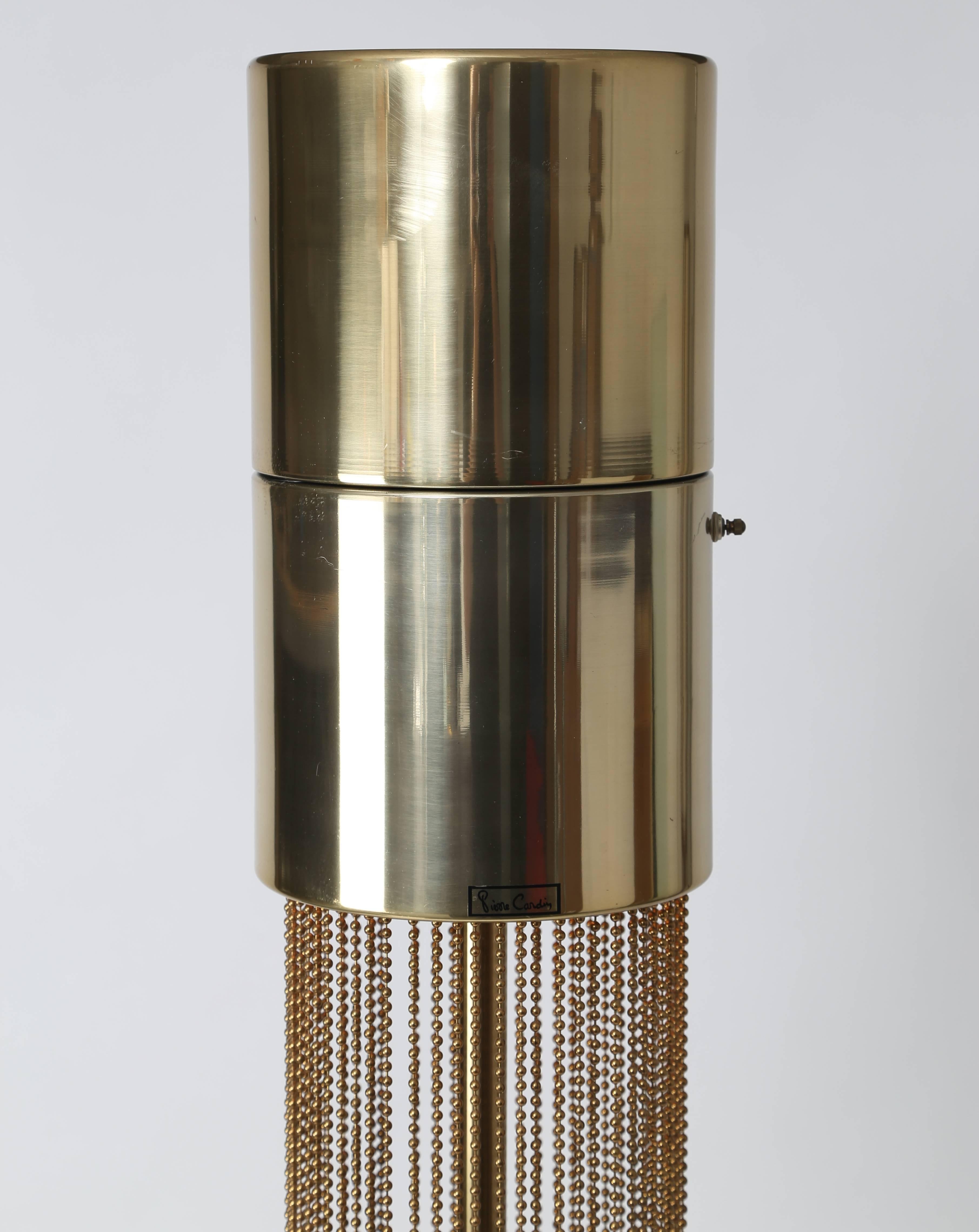 This quintessential 1970s floor lamp was designed by Italian-born French fashion designer Pierre Cardin. Circular forms at top and bottom are connected by a single pole surrounded by hanging brass beaded chains. Two standard-base bulbs are located