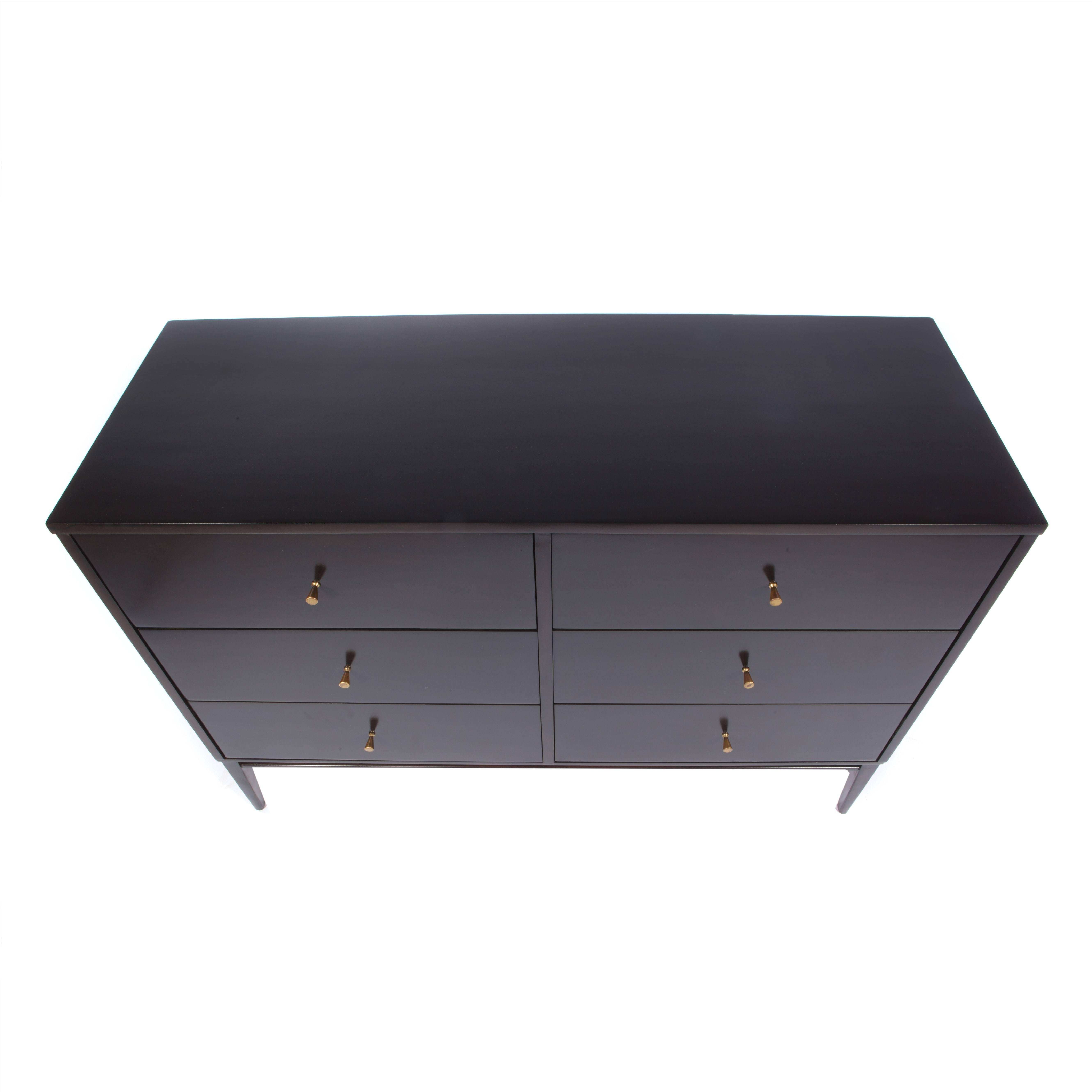 Six-drawer dresser supported by an elegantly tapered leg at each corner. Original conical brass pulls. The maple has been refinished in a hand-applied black satin lacquer. A bit of the woodgrain shows through this gorgeous finish. Foil 