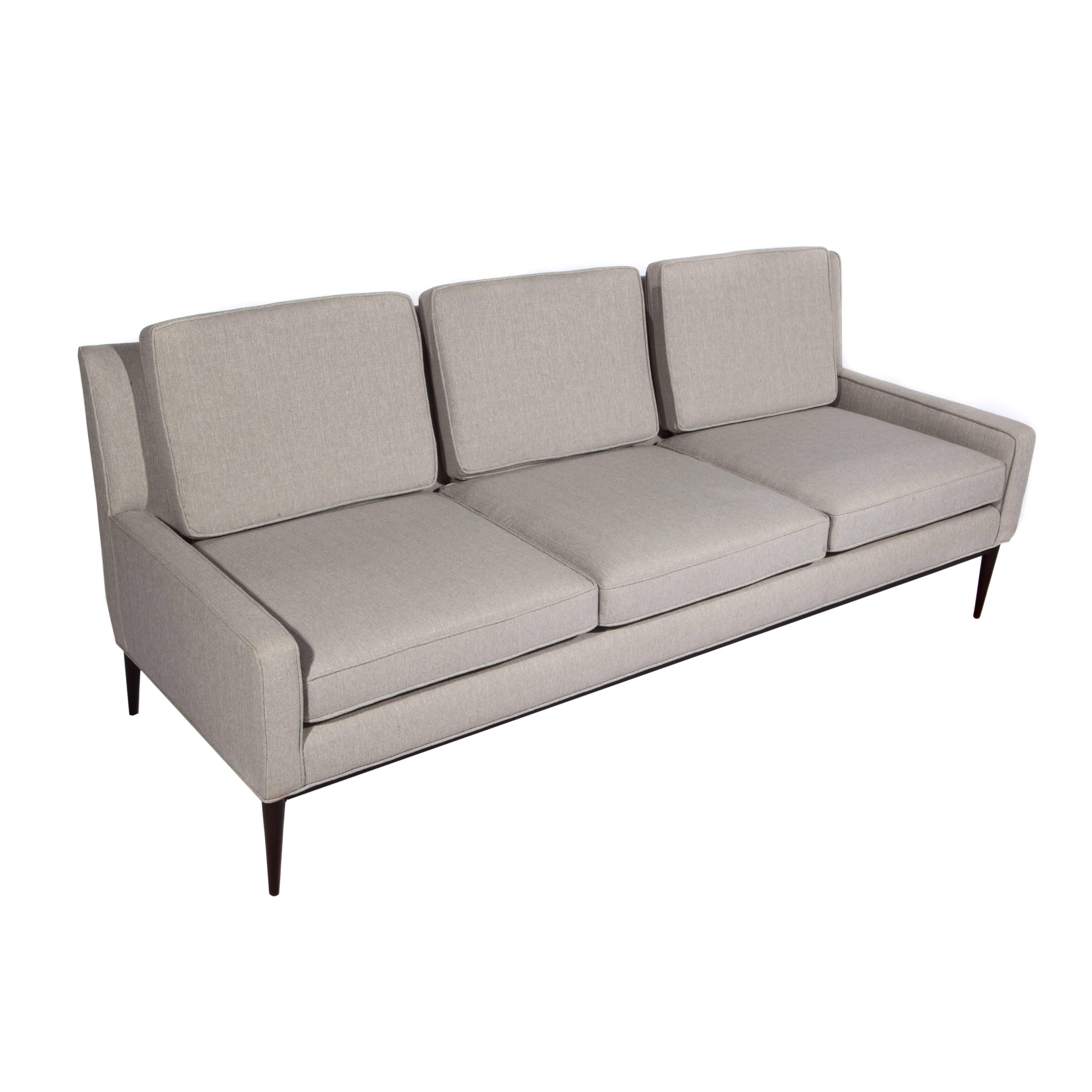 Chic, curved-back, three-seat 1950s Paul McCobb sofa floating on tapered and angled walnut legs. Newly restored and reupholstered in a light silver-gray woven fabric. Fabric swatch available. 

