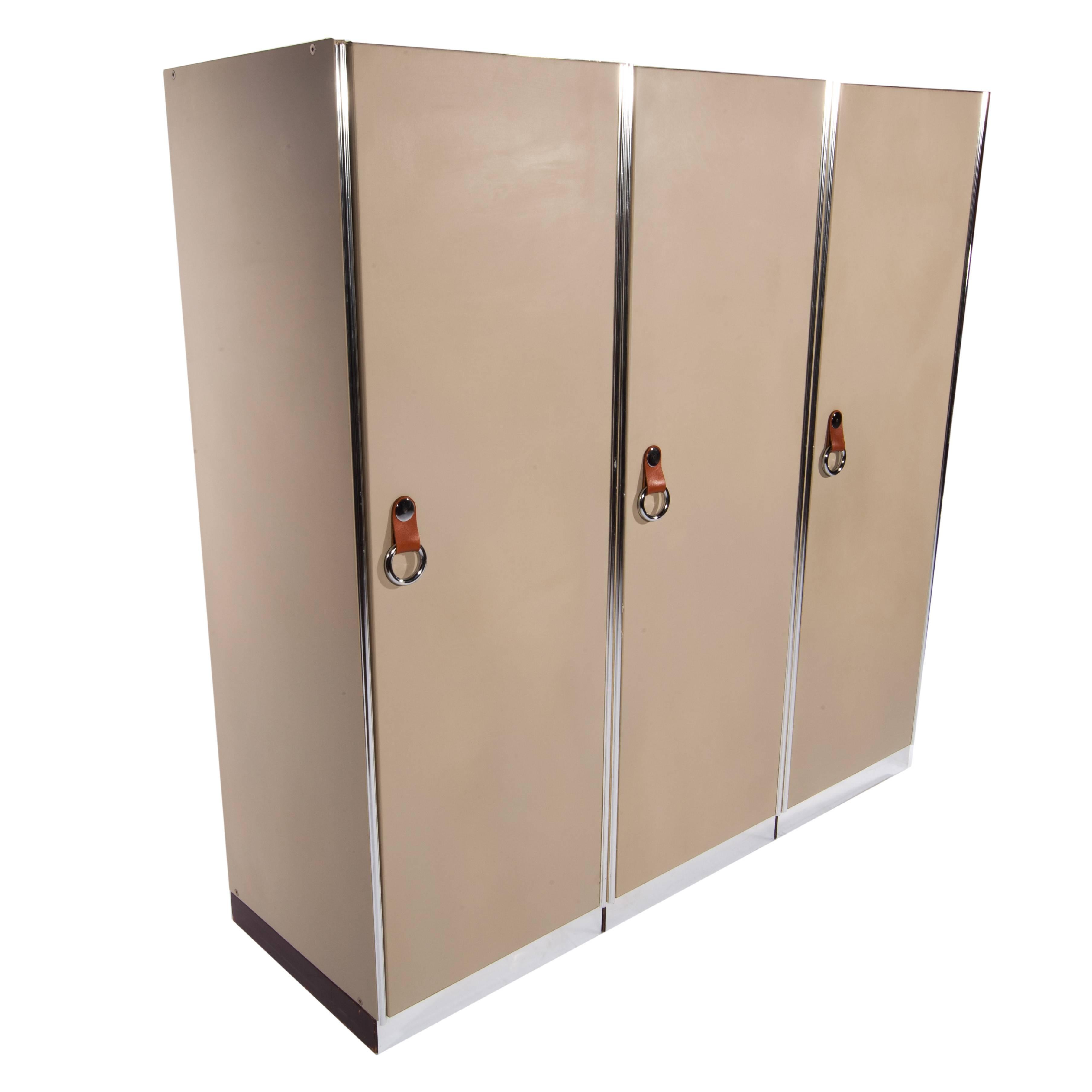A set of three tan, leather-front cabinets for i4 Mariani/Pace, circa 1970s. Each door opens on the left and conceals an upholstered interior with a single sliding track for clothes hangers. Cabinets feature leather and chrome handles and aluminum