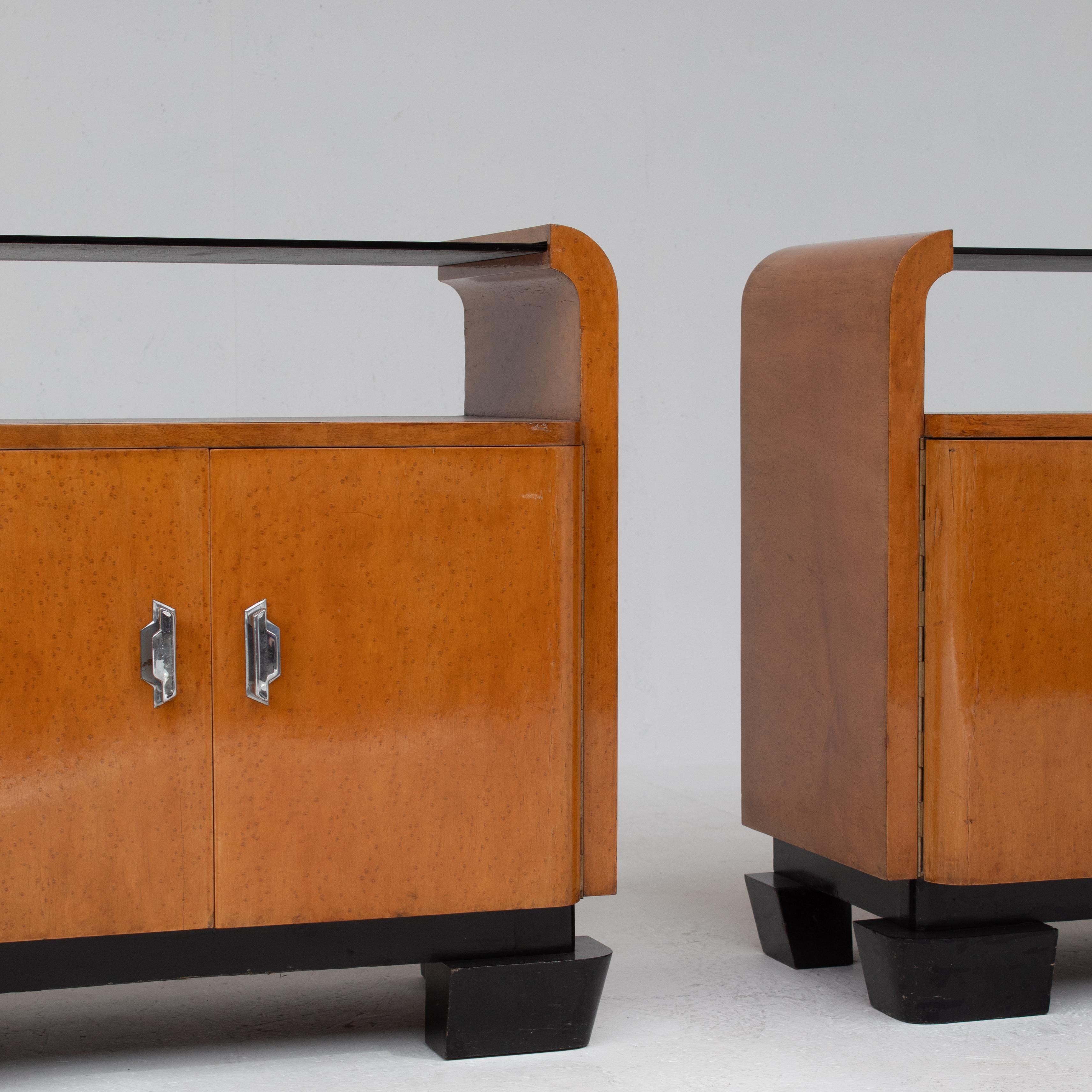 Ce magnifique ensemble de deux tables de nuit Art déco originales est une pièce rare des années 1930. Fabriquées en bois richement grainé, les tables de nuit Art déco reposent sur des pieds géométriques noirs. Les lignes classiques de l'Art déco
