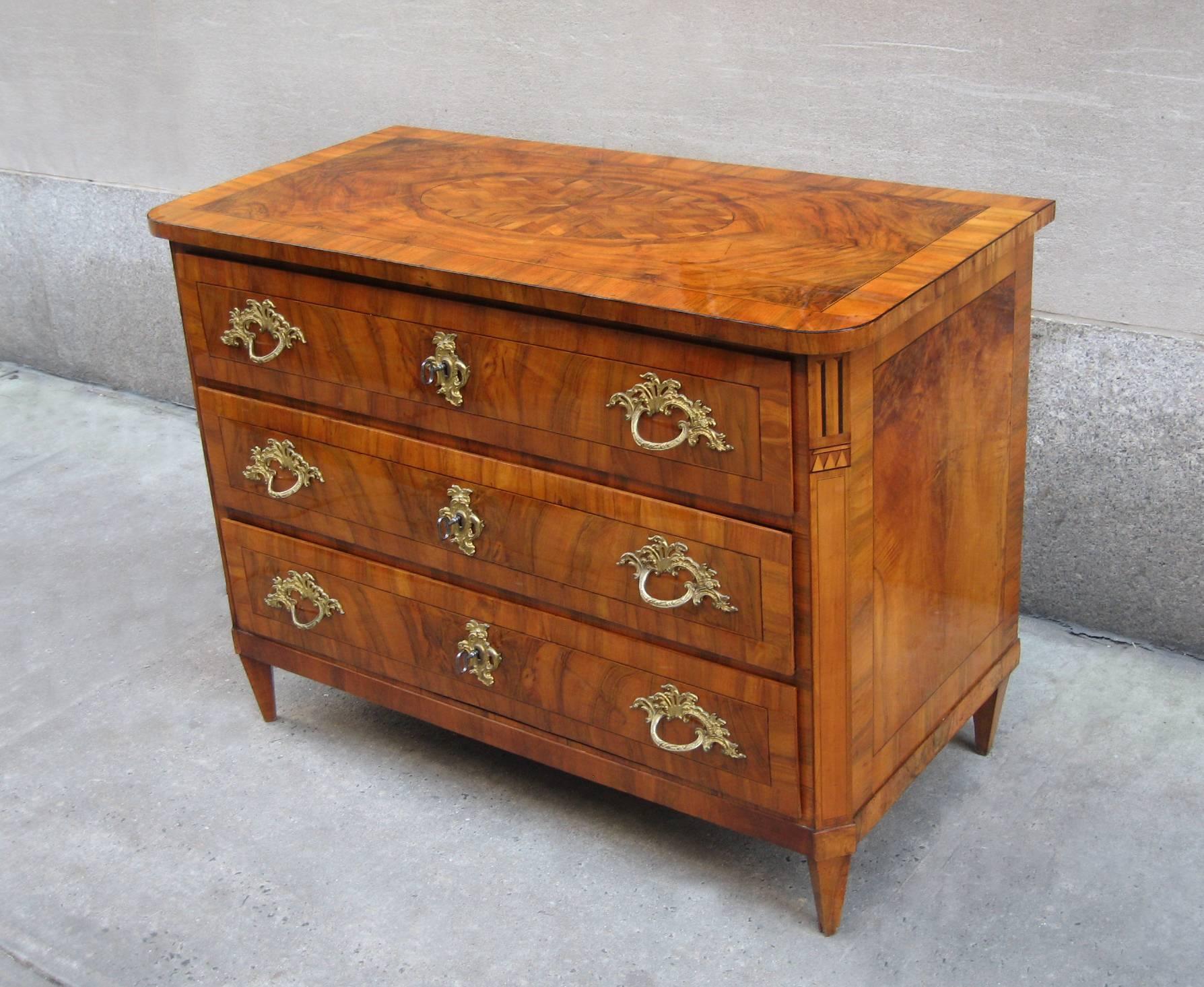 A fine Louis XVI period chest with three drawers from Dresden, Germany circa 1780. The top, front and sides feature walnut and walnut burl enhanced with an oval marquetry medallion on the top, ebony and fruitwood inlay on the square canted corners