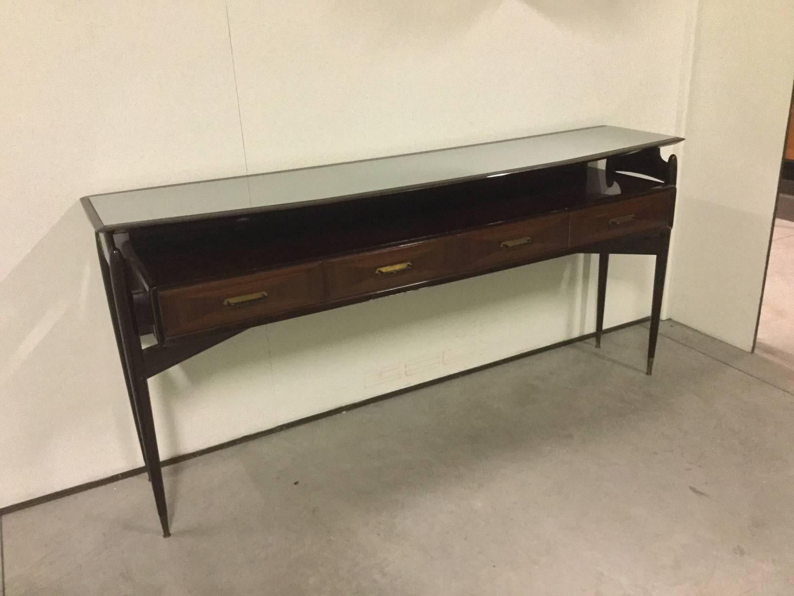 Beautiful console in mahogany wood with four drawers surmounted by a suspended opaline glass top, four legs linked by a cross-shaped with final brass at the feet. 
Italian manufactured in 1950 with assonance and similarity to Paolo Buffa works.