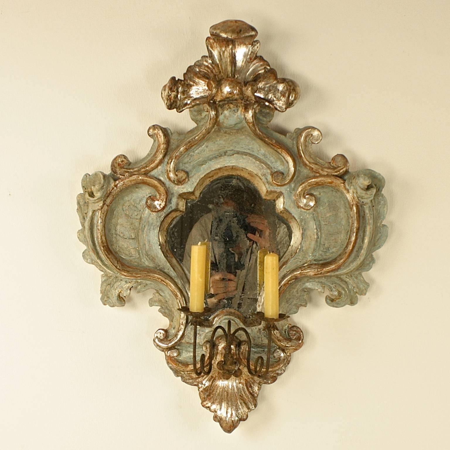 Pair of pale blue painted and silvered girandoles or sconce with two metal candle supports. The broadly symmetrical carving displays silvered scrolls and acanthus leaves contrasting with the blue surface decoration. The mirror glass and the silvered