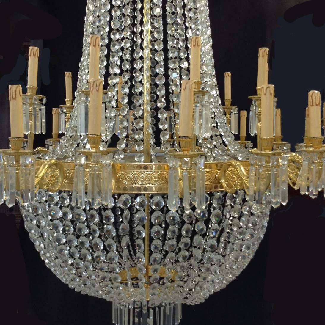A large imposing 10 foot high Empire style chandelier with an gilt bronze anthemion cast corona hang with chains of crystal drops, with a central gilt bronze band depicting guilloche and paterae, supporting 20 scrolled, reeded and foliate cast