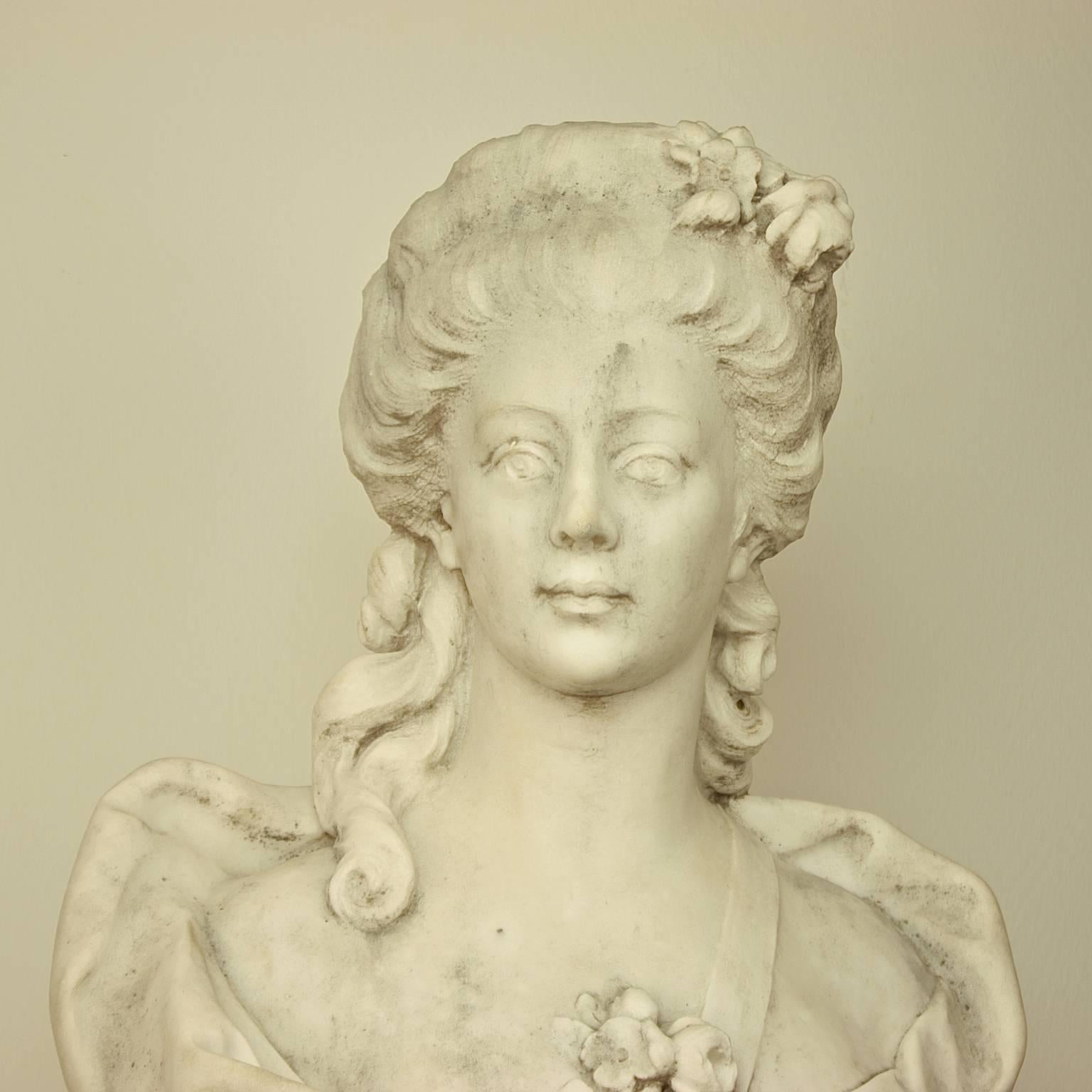 French white Carrara marble bust of a young lady in the style of the 18th century. A beautifully carved and sensual marble bust of a young woman who is 
facing half right. Her wavy hair is swept back from her face and dressed with a garland of
