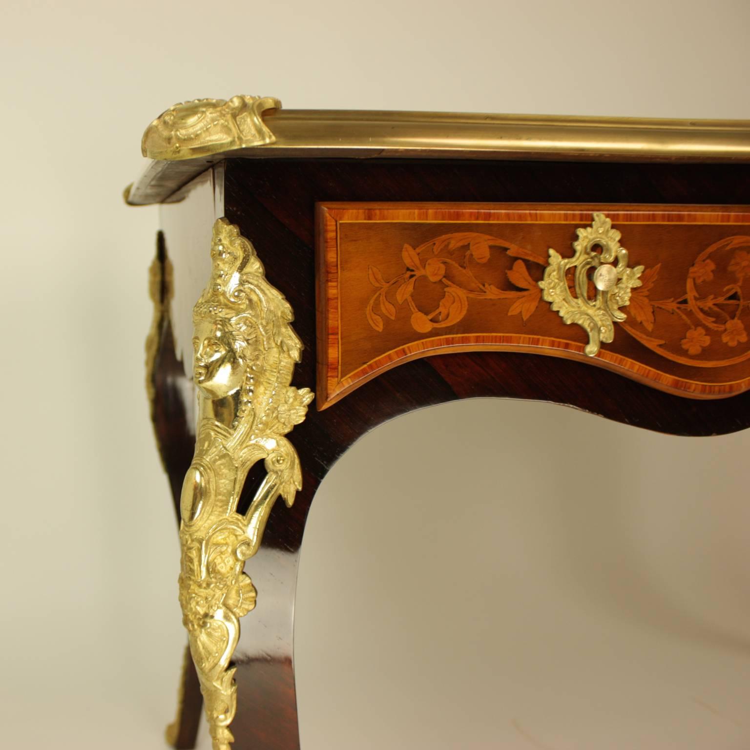 A 19th century gilt-bronze mounted and marquetry desk of freestanding form. With a brass banded rectangular top inset with a fine marquetry surface depicting a central and corner cartouches inlaid with stylised foliate, above three frieze drawers,