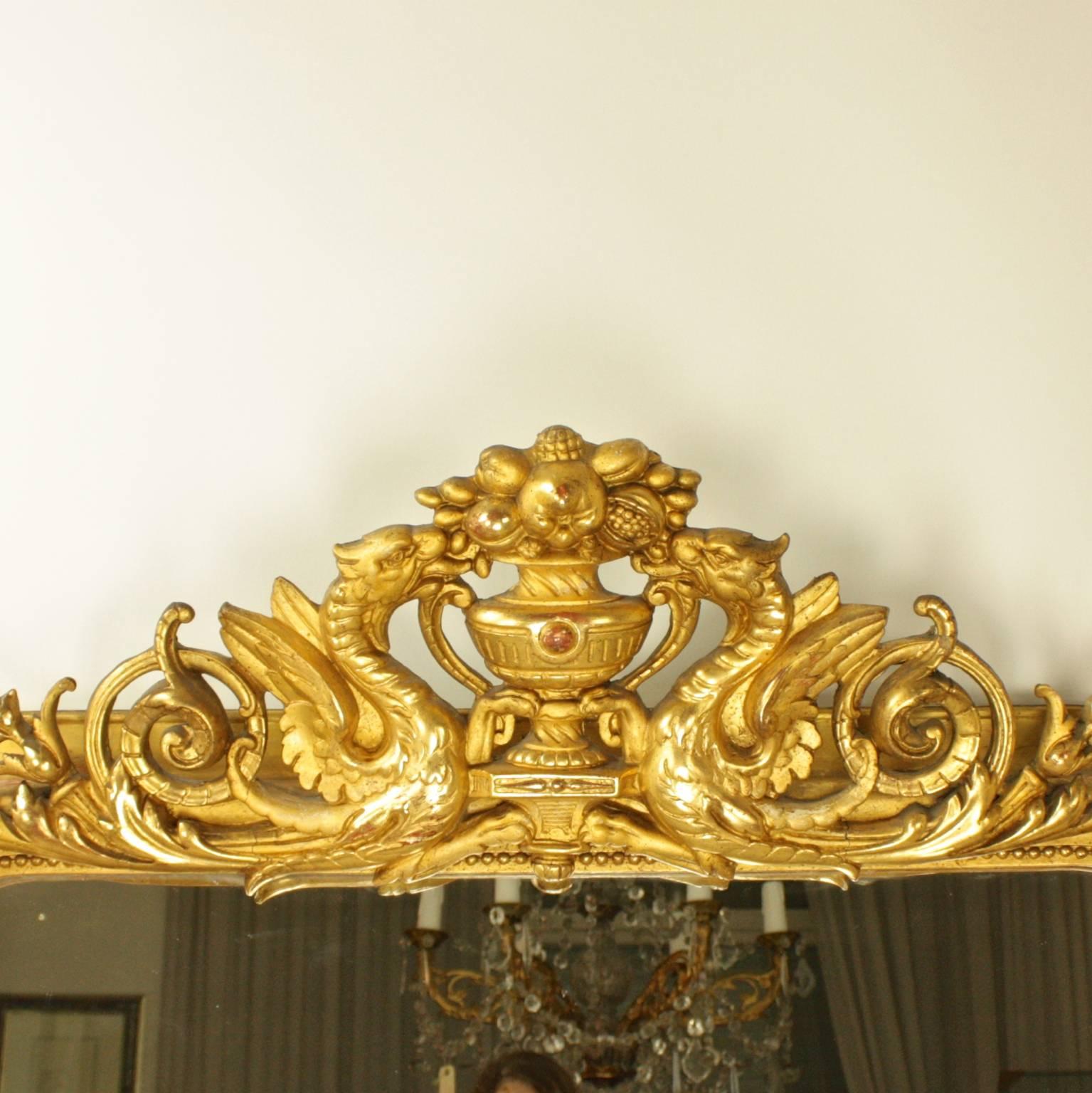 A large  19th century French giltwood mirror, the large rectangular plate surmounted by a pierced cresting carved with a central vase of flowers and flanked by two winged gryphons: mythical creatures with the head, wings and claws of an eagle, and