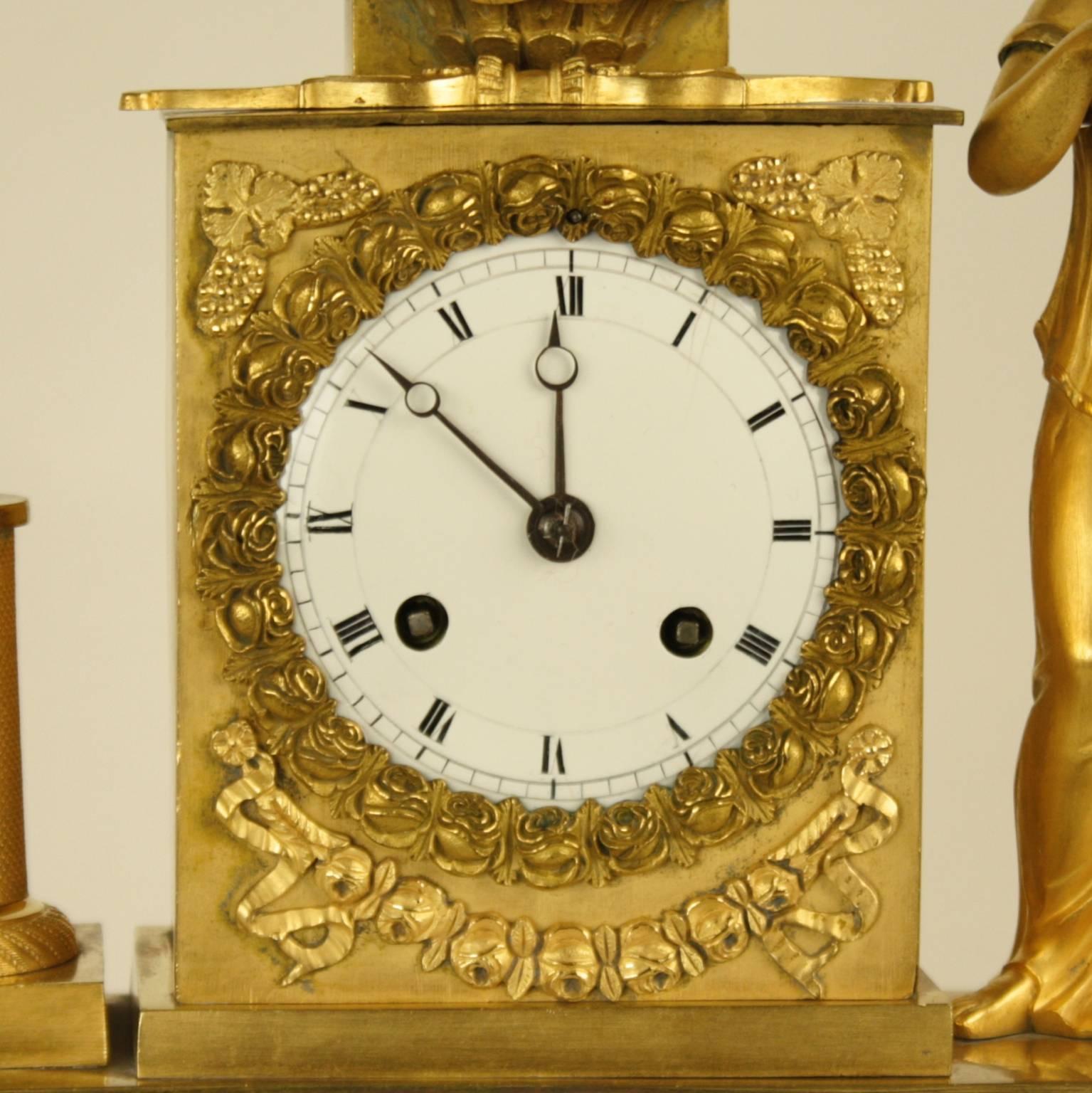 A fine French Empire mantel clock with a rectangular drum case surmounted by a wall fountain featuring a lion mask, flanked by the goddess Flora holding a flower in one hand and a bee the other - as Flora is not only the goddess of flowers but also
