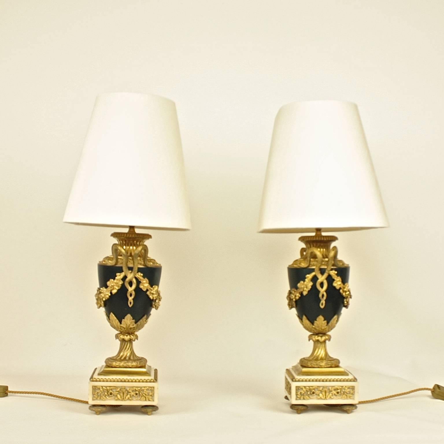 A pair of elegant early 19th century table lamps featuring Empire parcel-gilt bronze urns. The tapering dark green ovoid bodies flanked by serpent handles suspending wine swags, supported on stiff-leaf clasped waisted stems with laurel borders,