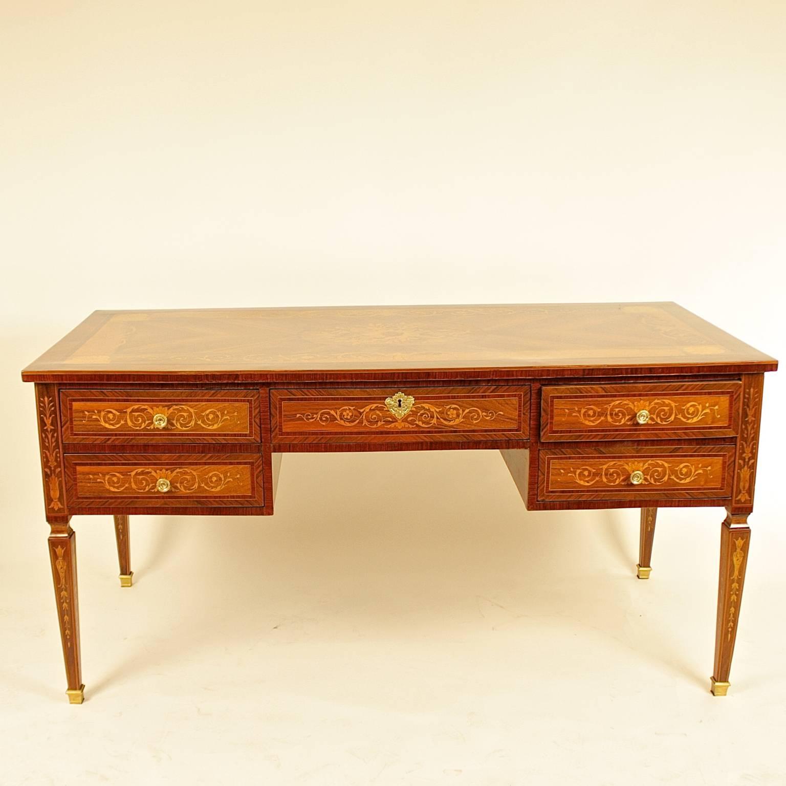 A freestanding writing table or bureau plat veneered in marquetry of fruitwood, walnut and other decorative woods, crossbanded in tulipwood. 
The rectangular quarter-veneered top centered by a foliate cartouche and corner cartouches, the kneehole