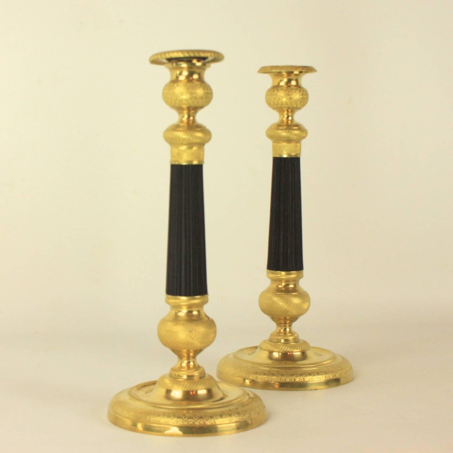 A pair of Charles X-patinated and gilt bronze candlesticks. The fluted, black patinated stem of each candlestick is highlighted on the top and bottom by an intricately sculpted pattern of beads and lines. The stem rests on a circular base accented
