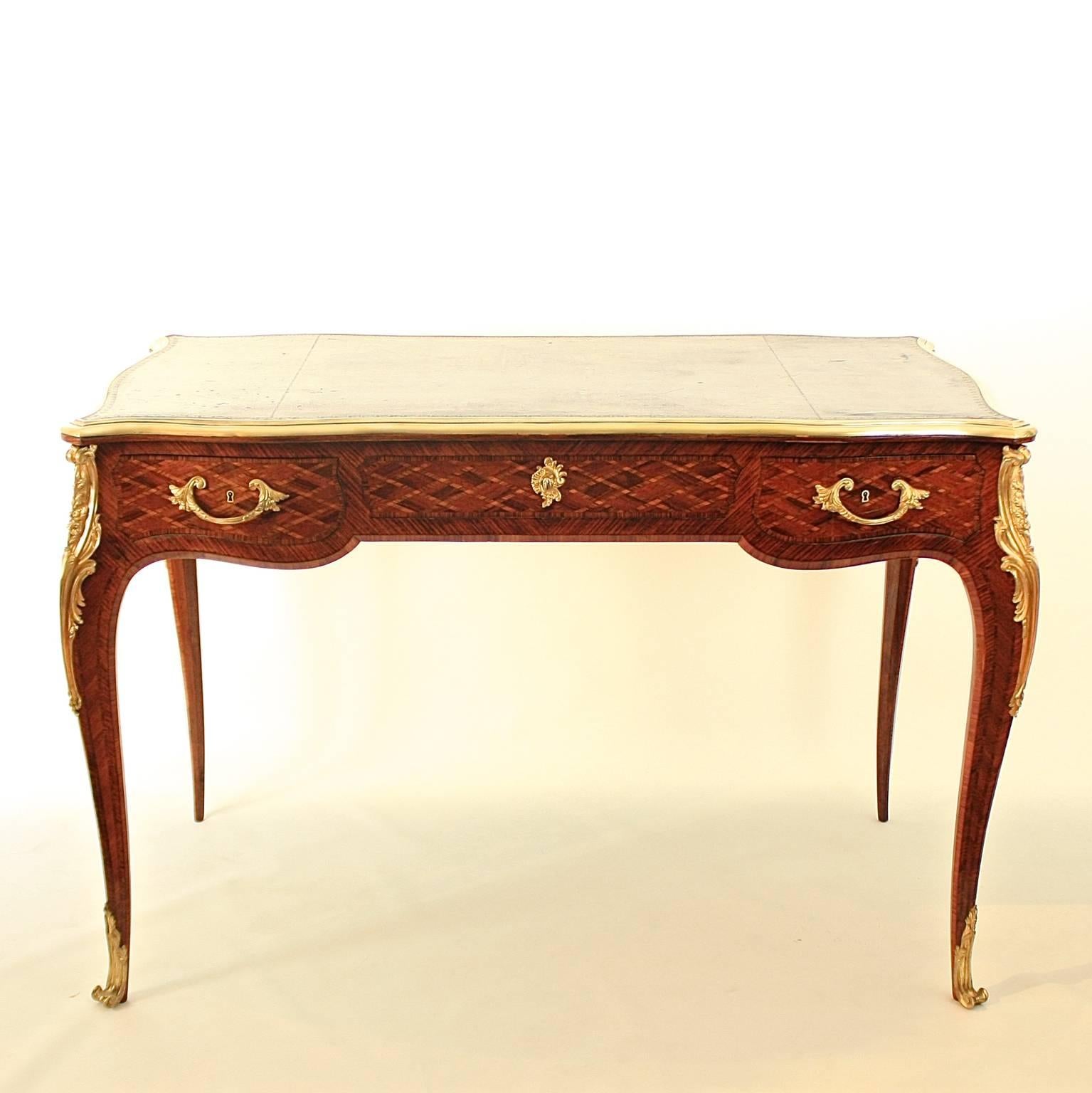A 19th century Louis XV style gilt bronze mounted marquetry bureau plat, with a brass banded tooled serpentine brown leather top with molded edge above three frieze drawers, each finely inlaid with trellis parquetry, the back decorated conformingly