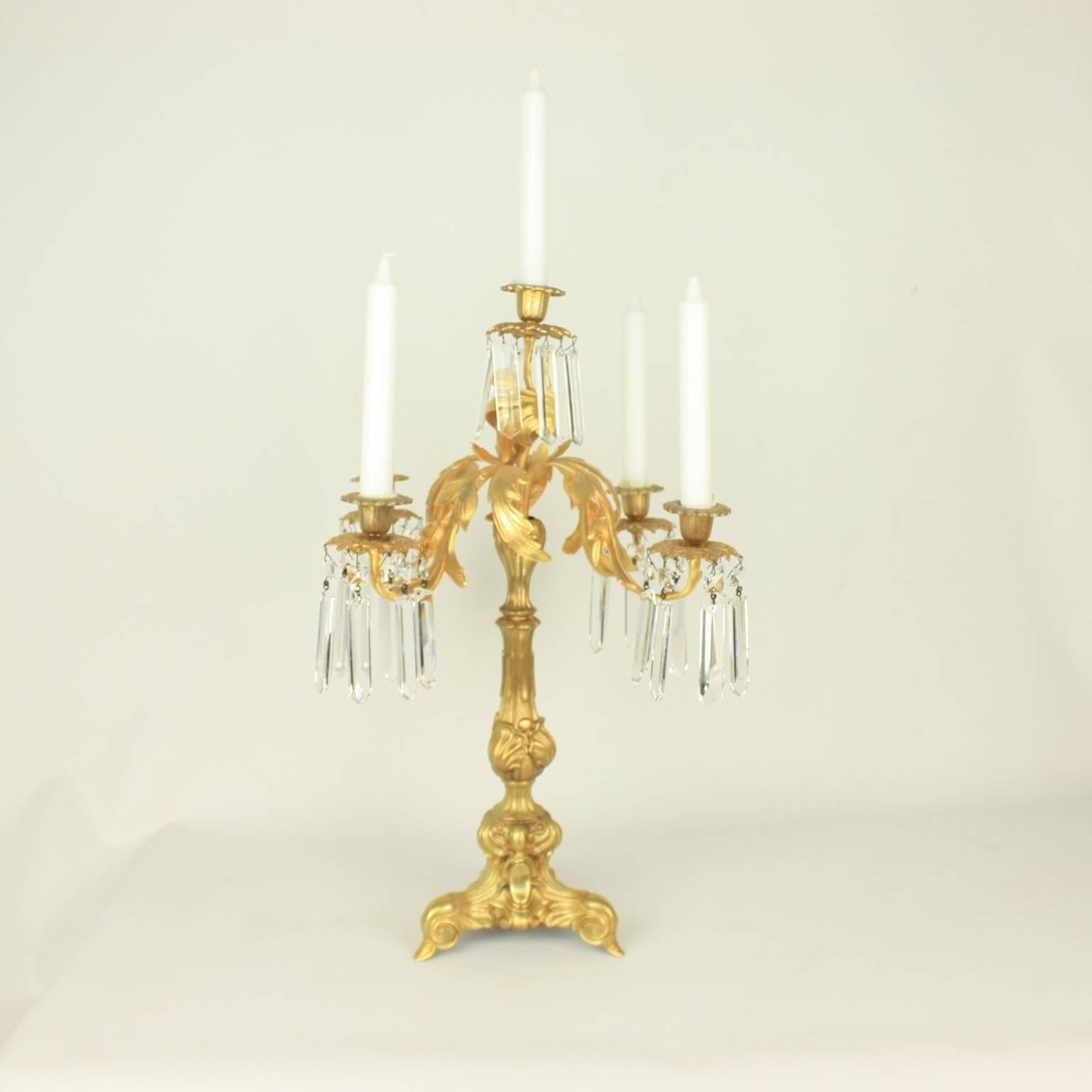 Coppia di eleganti candelabri in bronzo dorato in stile neo-rococò con cinque bracci a forma di foglie, che si dipartono da uno stelo a balaustro avvolto d'acanto e appeso a un prisma di cristallo, appoggiato su una base triforme.