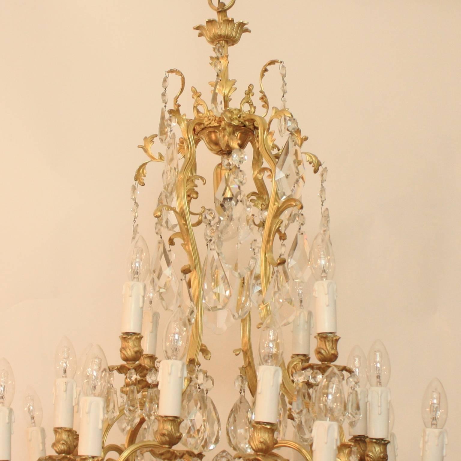 A rare and exceptional large 19th century French gilt-bronze chandelier with a central solid cut-crystal finial surrounded by an open gilt-bronze cage frame with three tiers of scrolled and fluted branches issuing altogether 20 lights, each with