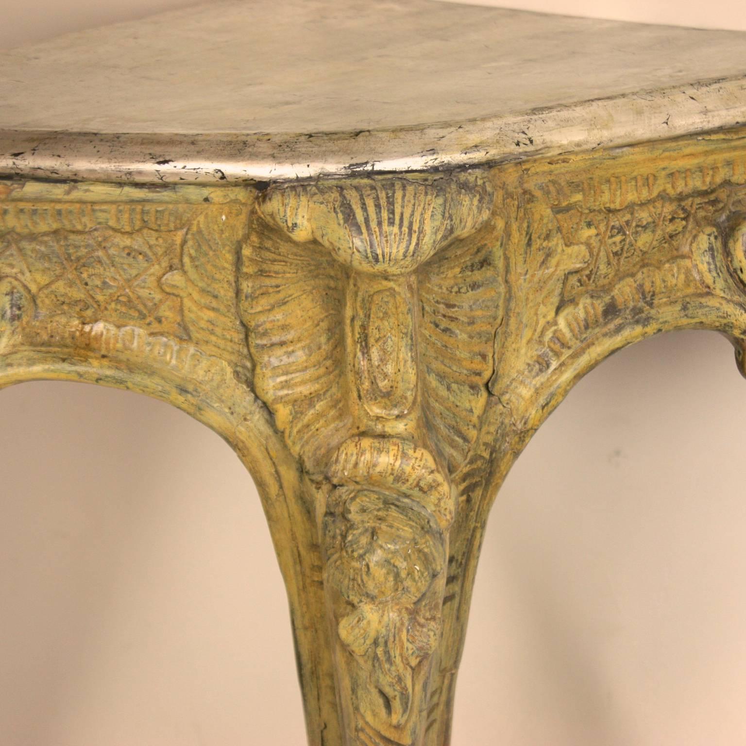 A pair of 18th century North Italian pale green carved corner console tables with a silvered top above a frieze carved with foliage rocaille and scrolls, on cabriole leg terminating in a scrolled foot. The warm yellowish green surface corresponds