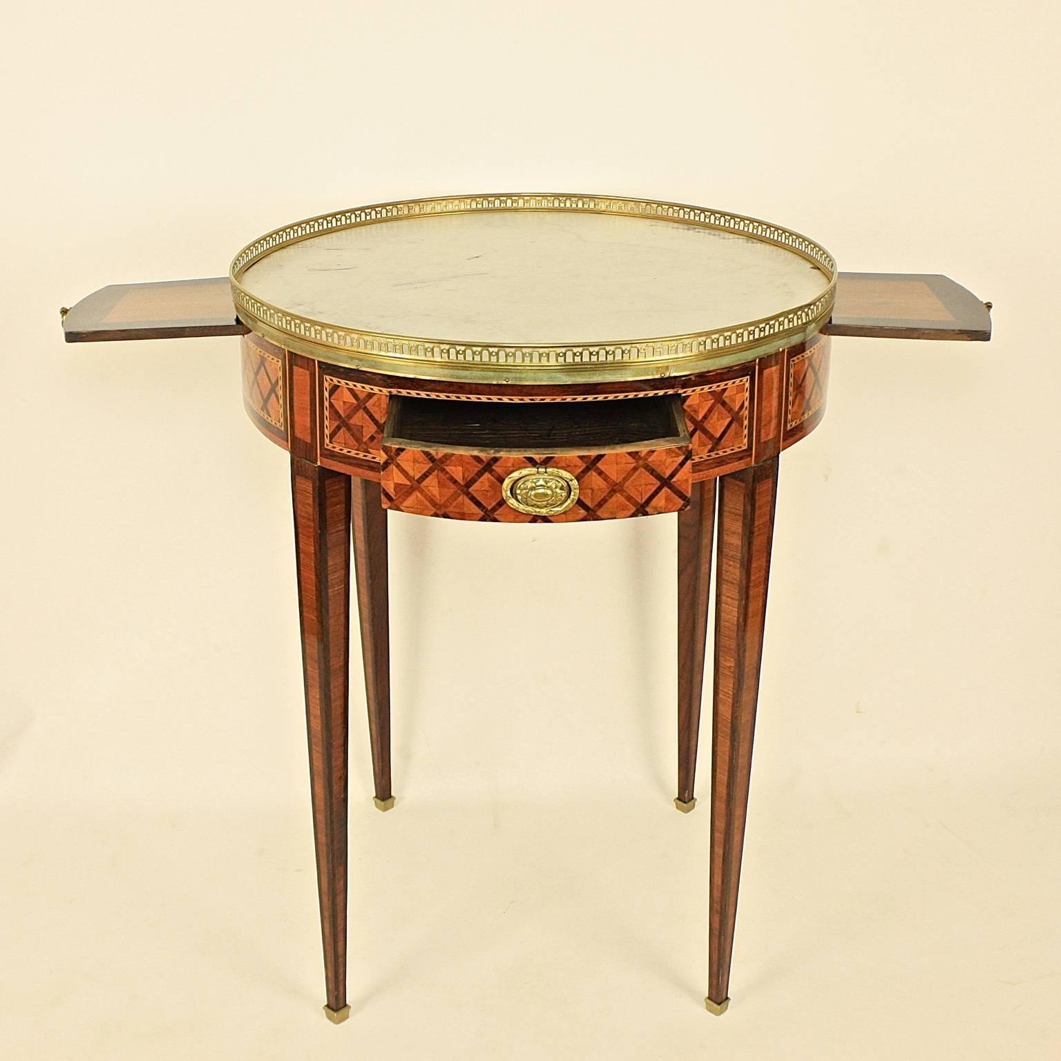A 19th century Louis XVI bouillotte table, with a white mottled round marble-top within a pierced brass gallery, above a frieze with kingwood and tulipwood trellis work marquetry, two drawers and two candle slides, on square tapering legs with