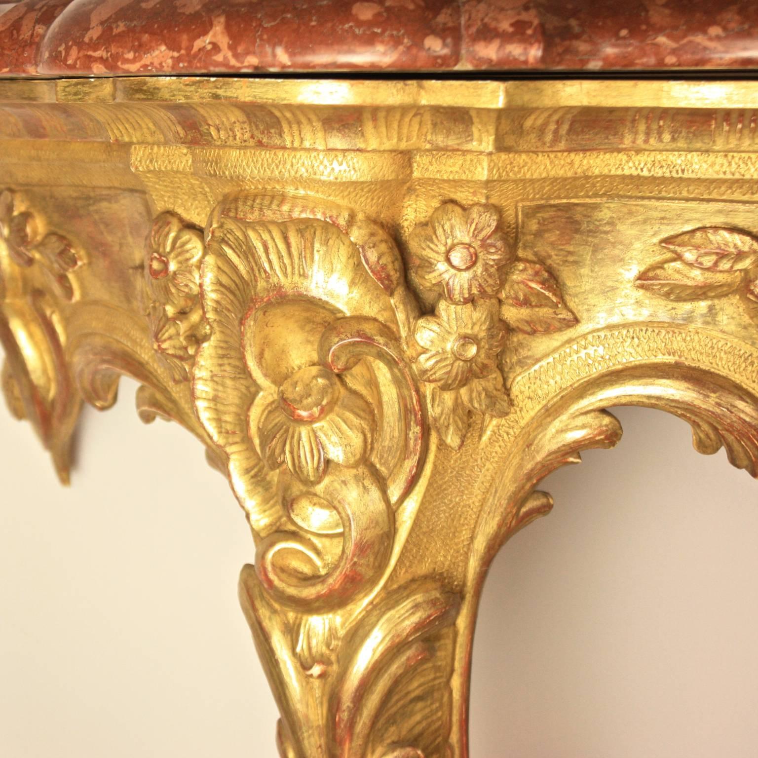 An Italian early 20th century Louis XV style giltwood console table with a red Breccia marble top of serpentine form above a pierced frieze and stretcher carved with rocaille, flowers and leaves on cabriole legs similarly carved. Water gilding of