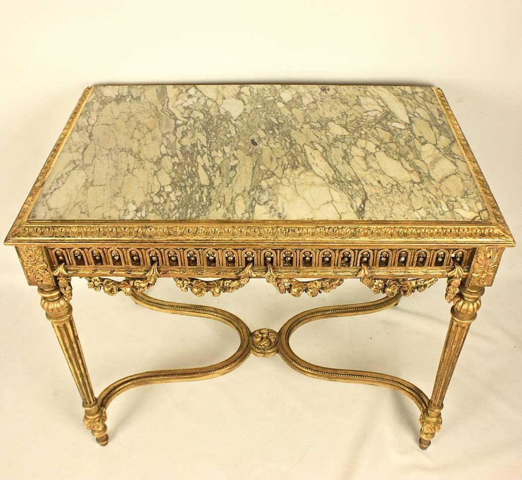 A 19th century giltwood center table with an inlaid white and grey mottled marble-top. The rectangular top is framed by a leave carved cyma. The pierced frieze adorned on each side by foliate swags that move in and out of the frieze.
The table is