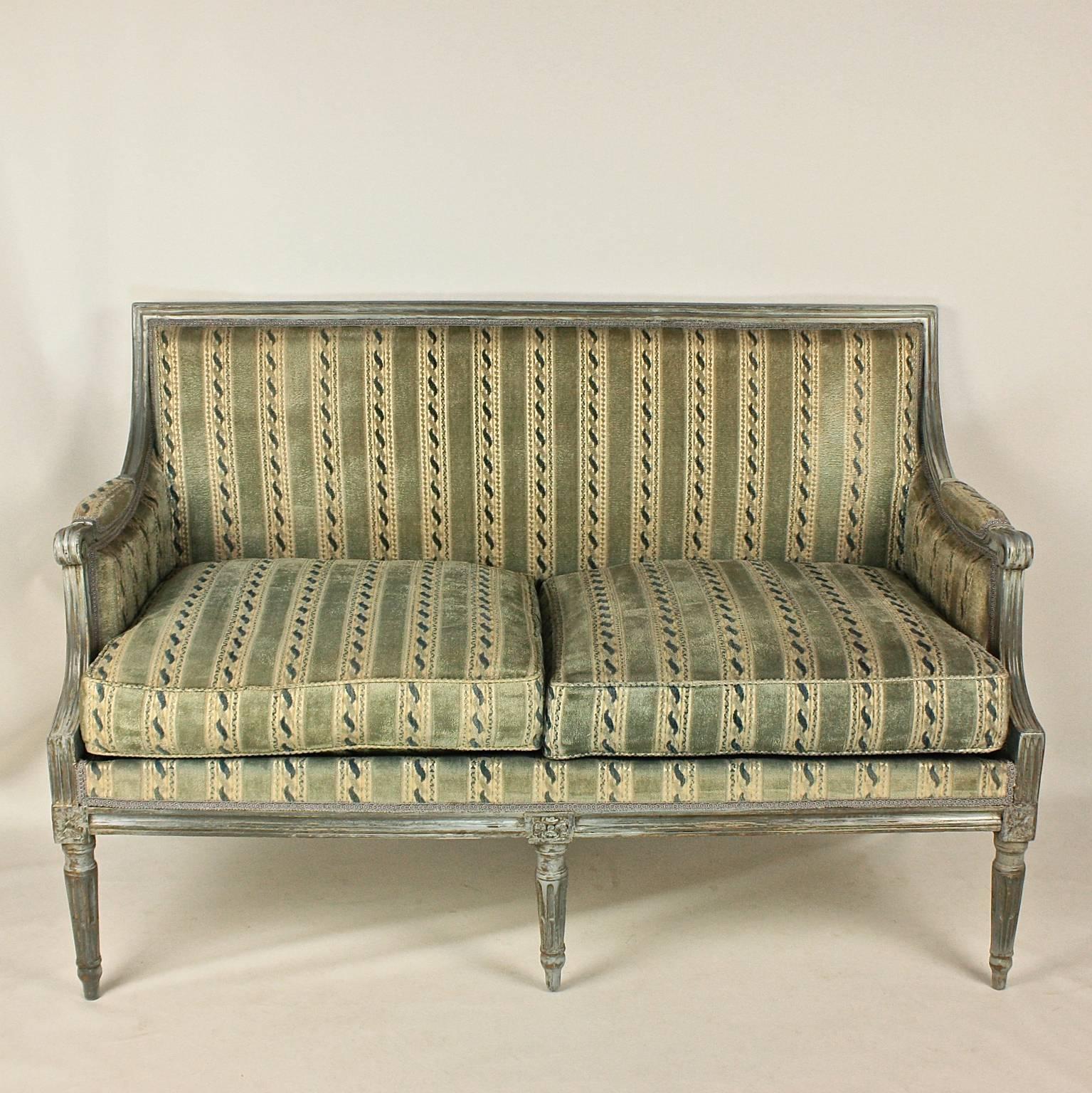 An 18th century Louis XVI blue or grey painted sofa with a rectangular padded back, the top-rail carved with plain moulding, with padded sides and scrolled supports, a double cushioned seat and each block of the seat rail headed by a patera on round