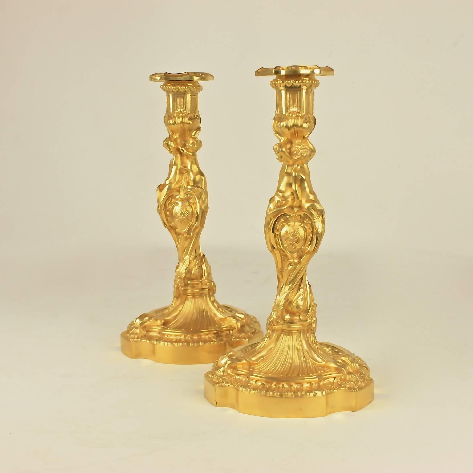 A pair of finely chased ormolu candlesticks with twisted stems of swirling, asymmetrical Rococo form, the three-sided stems with three figures of children each of elongated, graceful and refined posture, sitting on large cartouches representing the