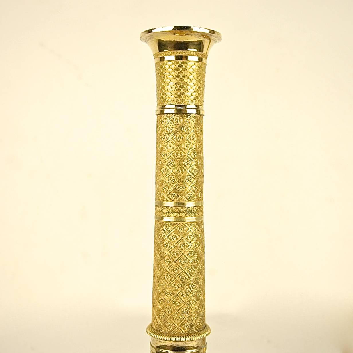 A fine pair of Empire candlesticks, each richly ornamented with fish scale ornament and intricate trellis work. Each candlestick rests on a circular base chiseled with a ring of laurels, gadrooning and trellis work. The decor is very intricately