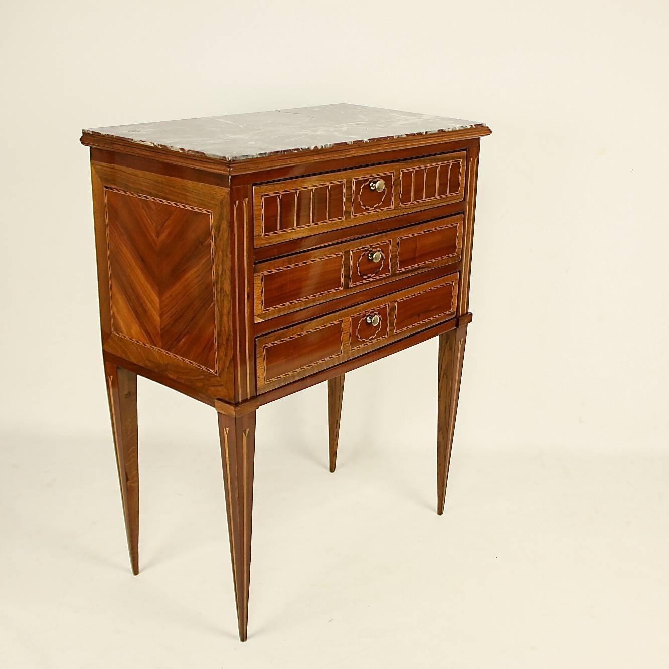 Late 18th century Louis XVI side table or ' Table Chiffoniere' in the manner of Nicolas Petit (1732-1791), with a rectangular inset dark red marble top above three drawers, decorated with fillet marquetry, the sides and square tapering legs inlaid