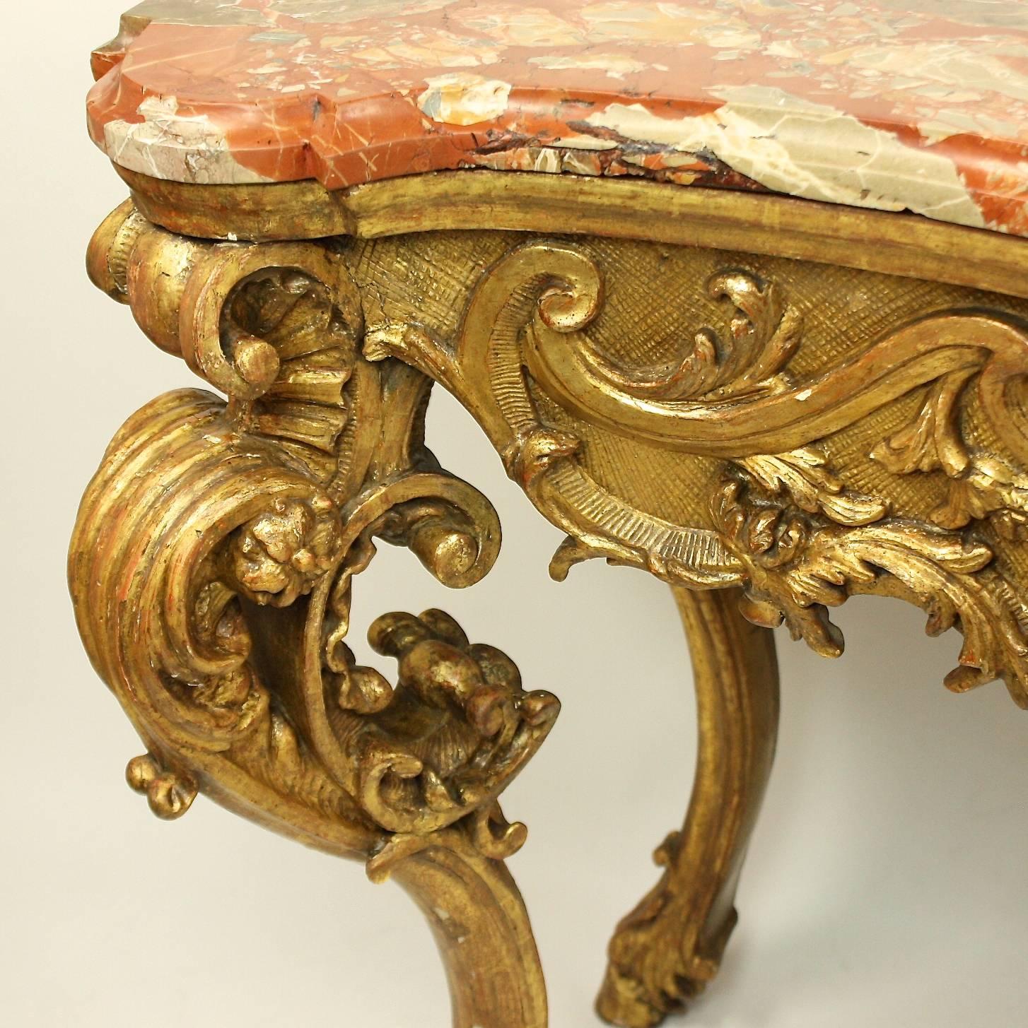 An impressive early 18th century Regence giltwood console table with the original moulded breccia marble top in red and white, above a serpentine pierced frieze carved with a central finely carved acanthus leave arrangement above a scallop shell