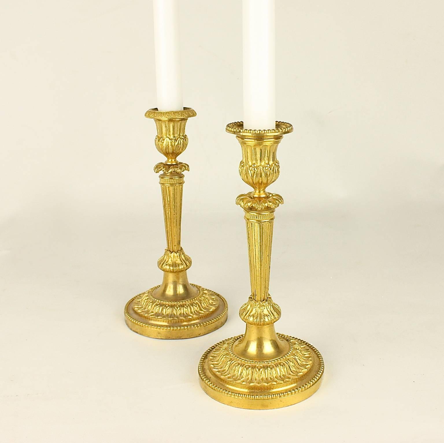 A fine pair of 18th century Louis XVI ormolu candlestick with a fluted stem topped by a ring of prominent leaves supporting the fluted socket, chiseled with foliage. The removable nozzle heightened with fine pearls, resting on a round base richly